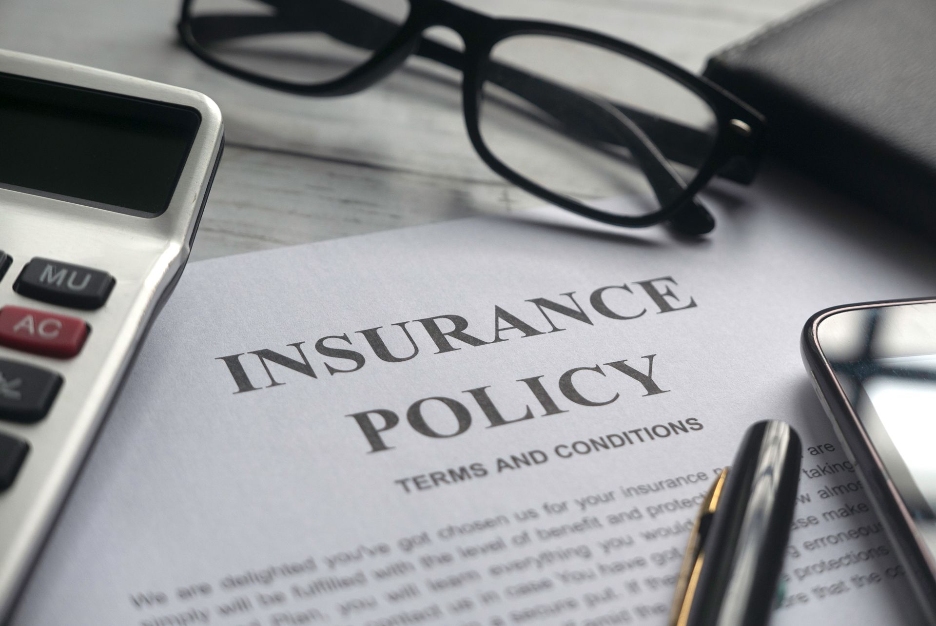 Insurance policy document with calculator, eyeglasses, and pen on a desk