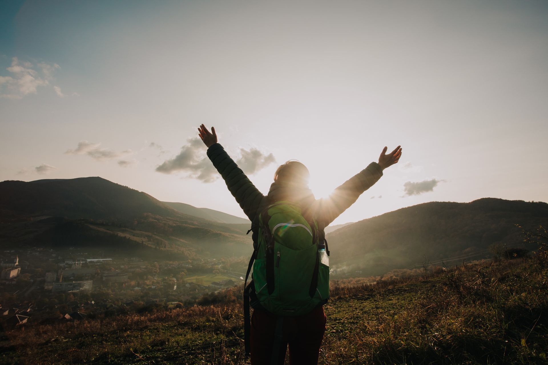 Person with backpack raising arms on a mountain trail at sunset