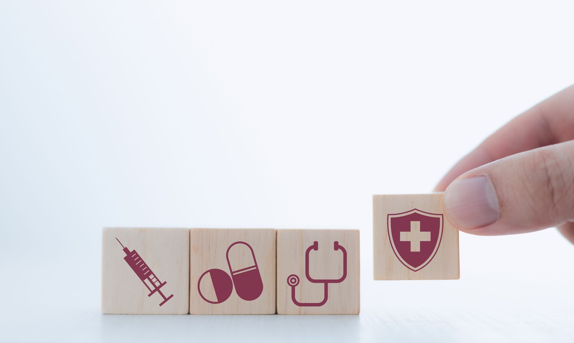 Hand placing a medical cross block beside other health care blocks, including syringe and pill icons