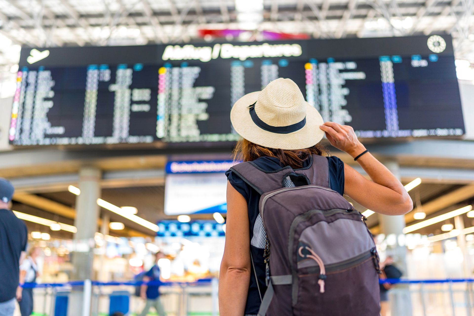 Traveler with backpack and hat reading airport departure board