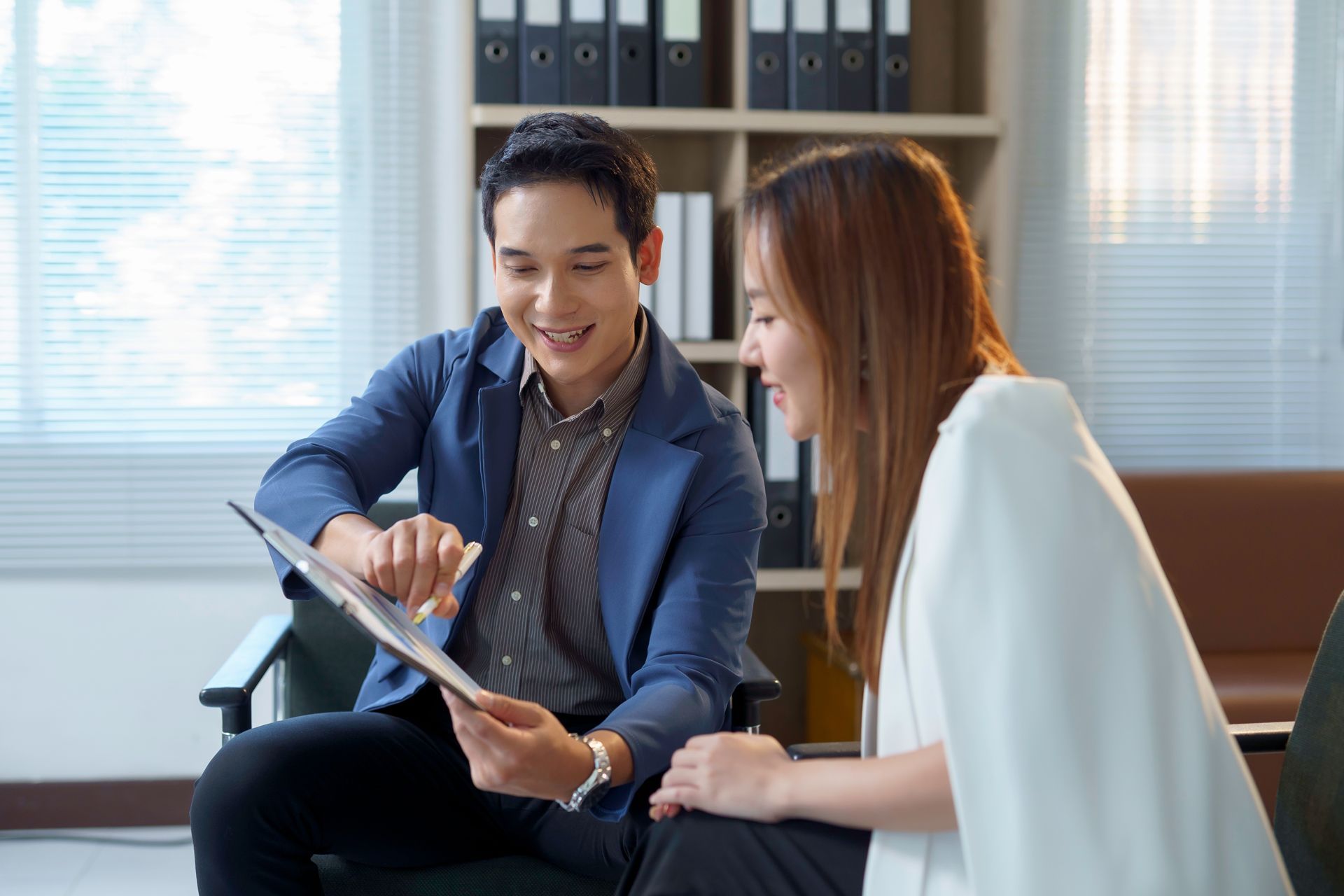 Two colleagues in a bright office reviewing a tablet together on a couch