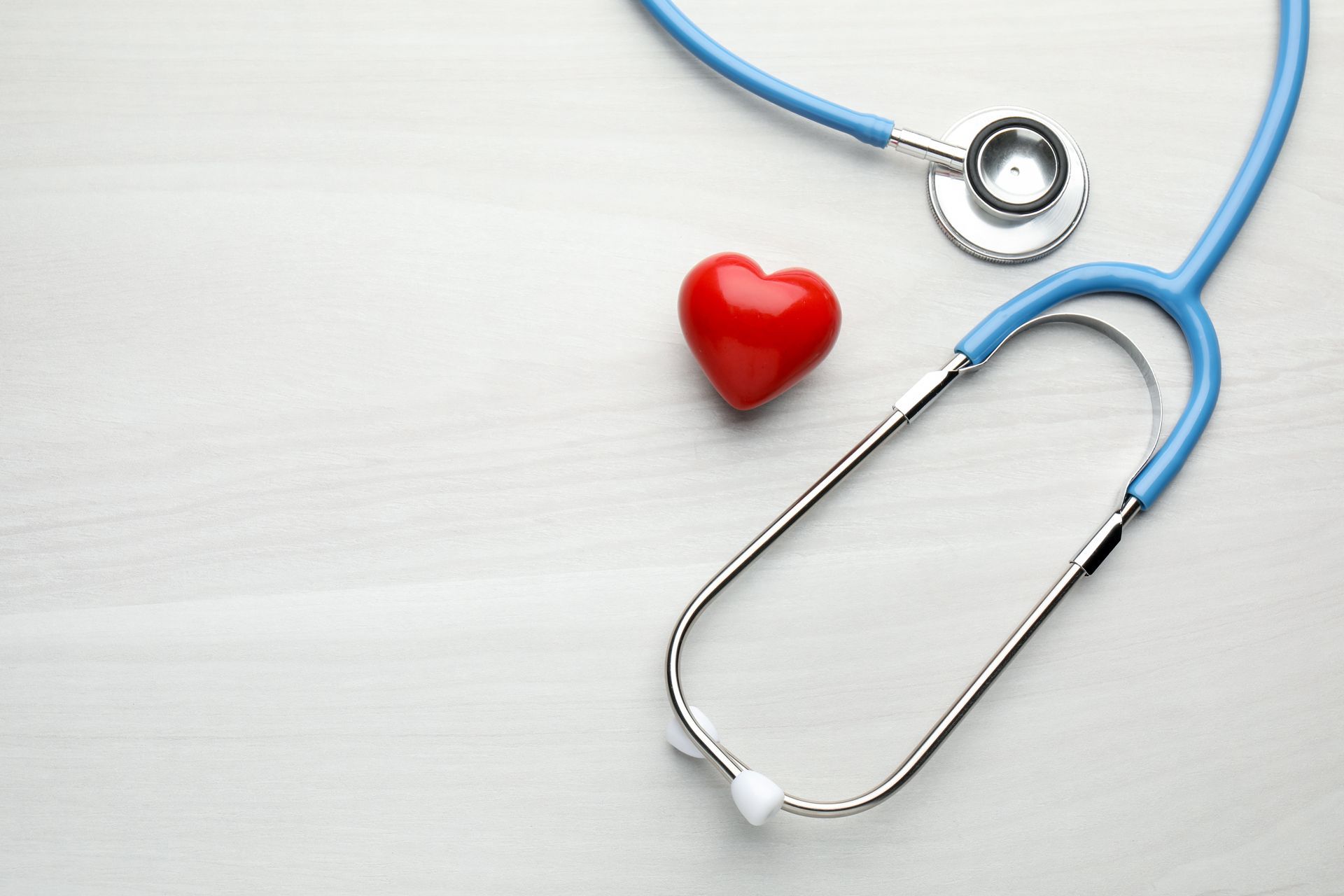 Blue stethoscope beside a red heart on a light background