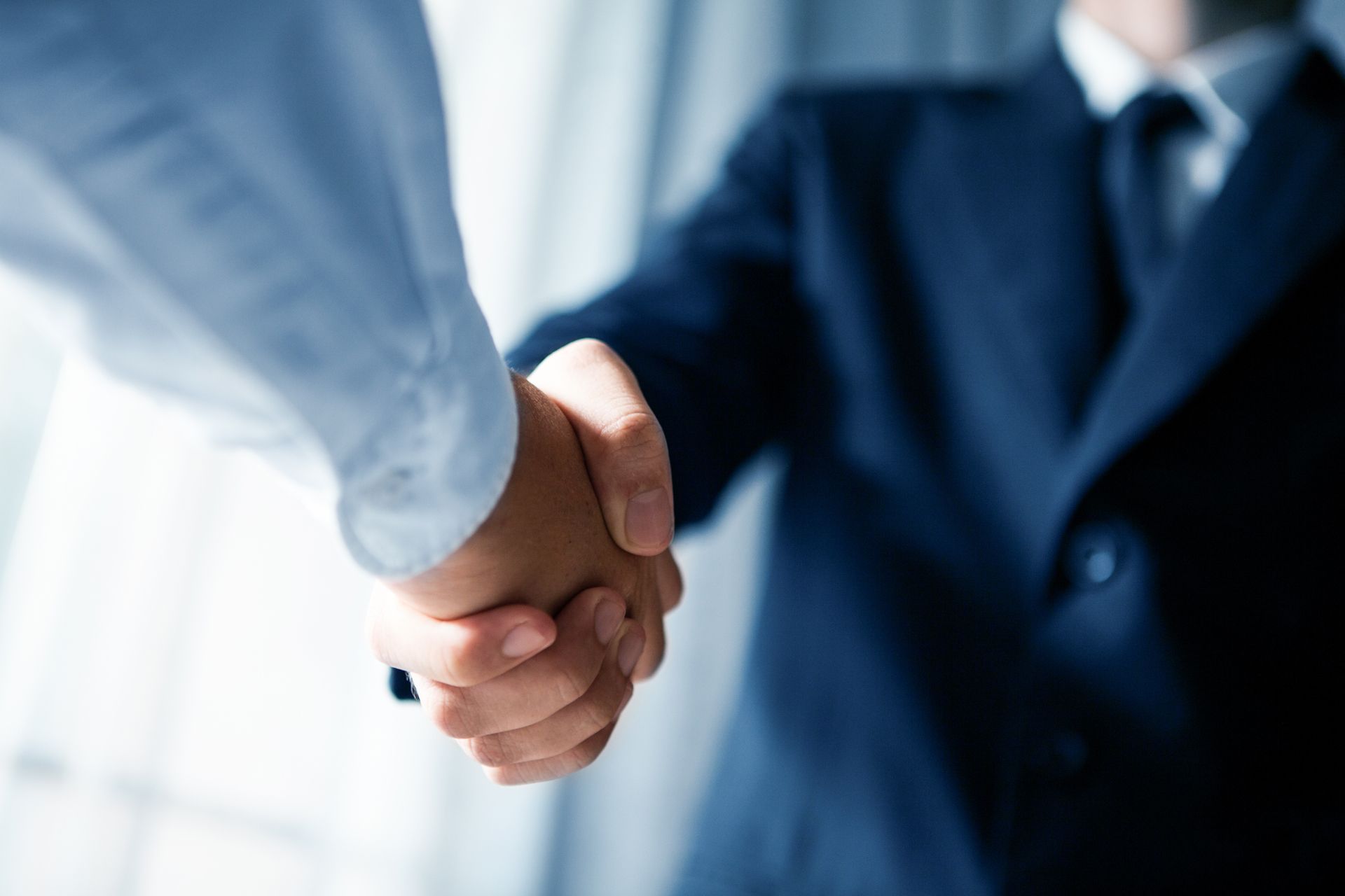 Two people shaking hands in a business setting, one in a light shirt and one in a dark suit.