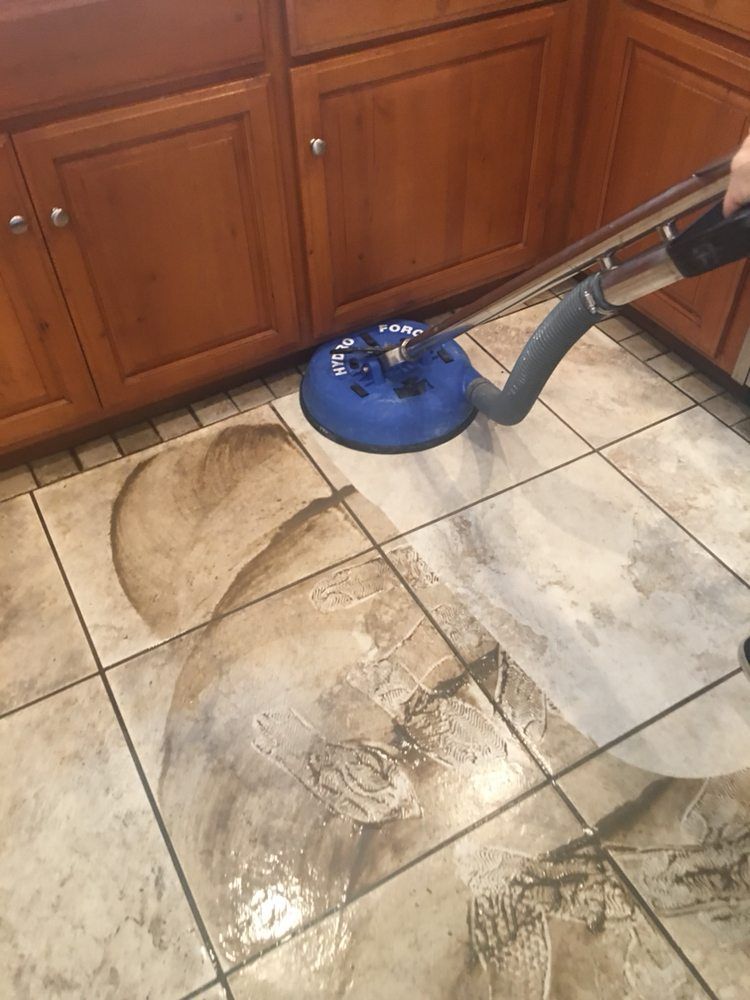 A vacuum cleaner is cleaning a tile floor in a kitchen.