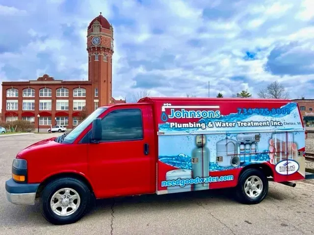 A red johnsons plumbing and water treatment van is parked in front of a building.