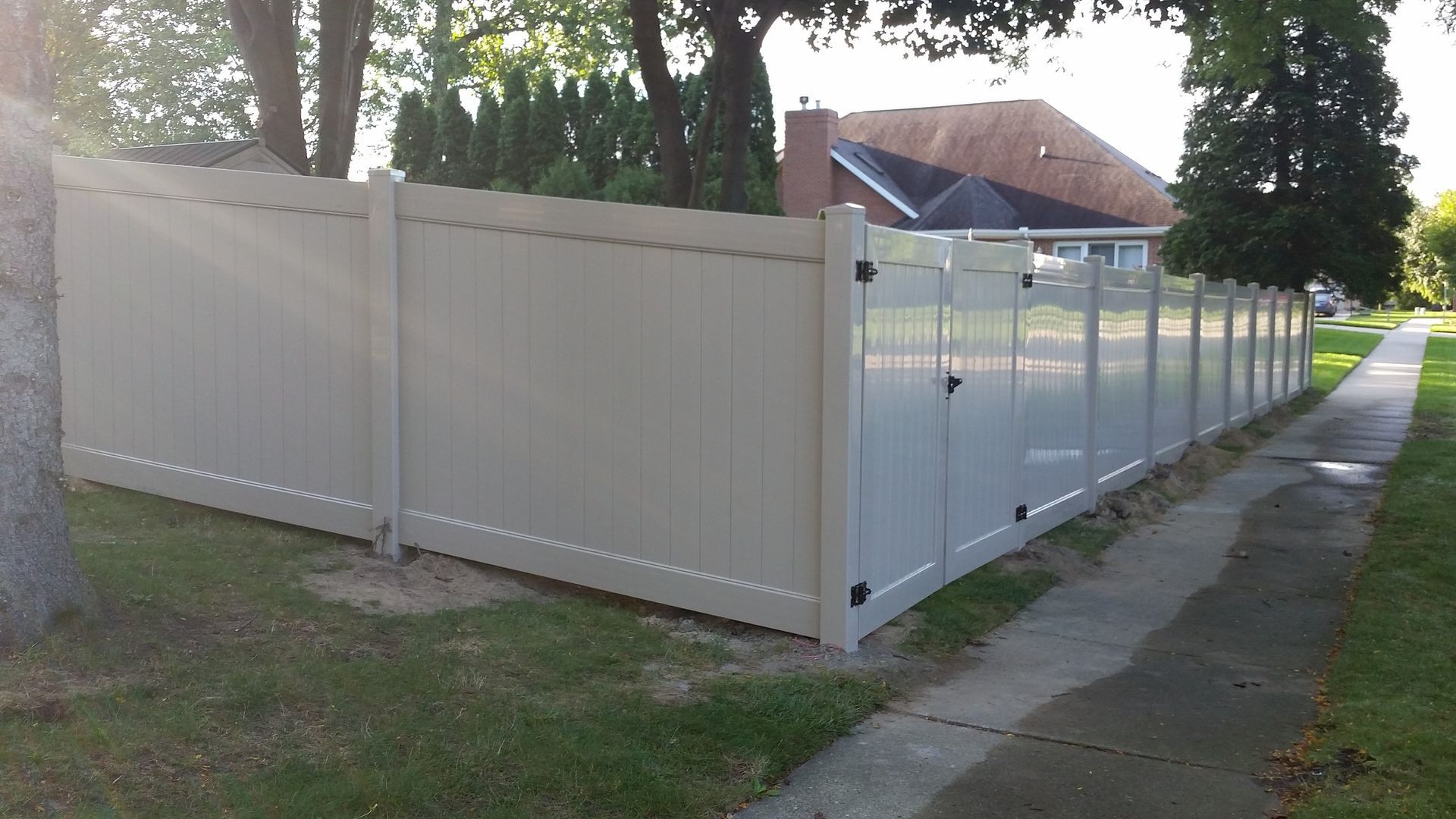 Beige vinyl fence around a yard, next to a sidewalk and street.