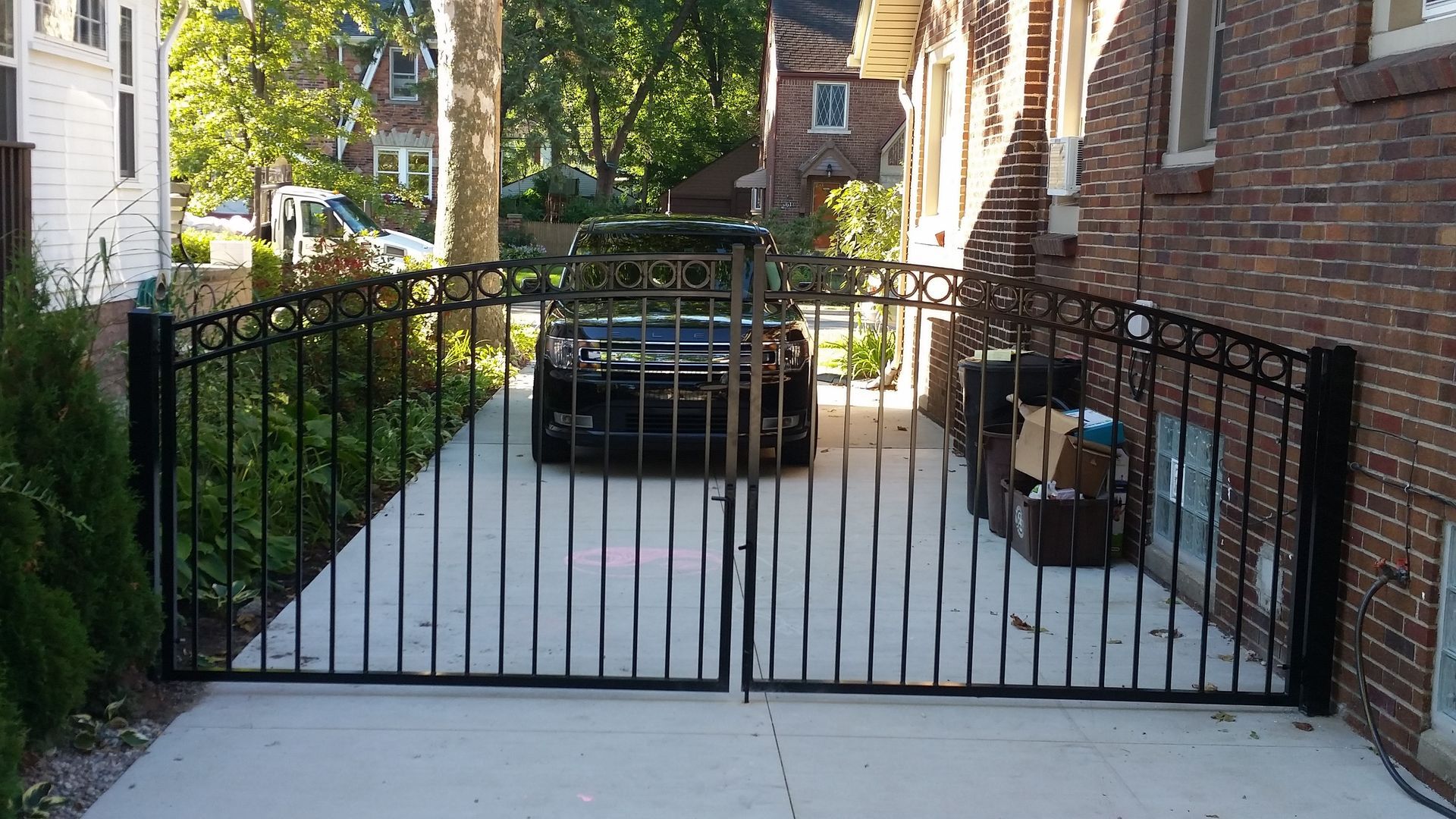 Black wrought-iron driveway gates open to a paved area with a car parked in the center.