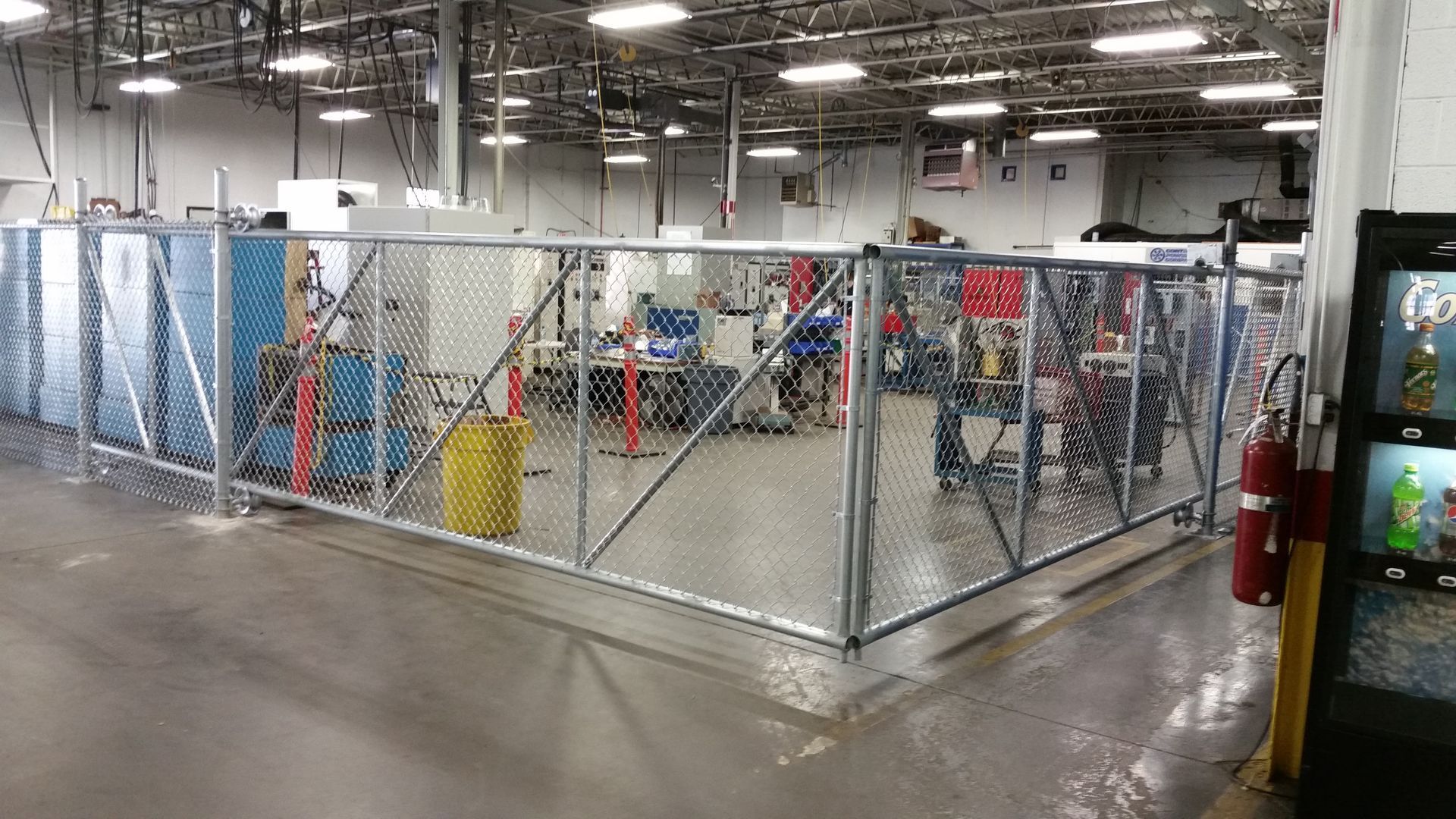 A metal chain link fence encloses a work area inside an industrial building.
