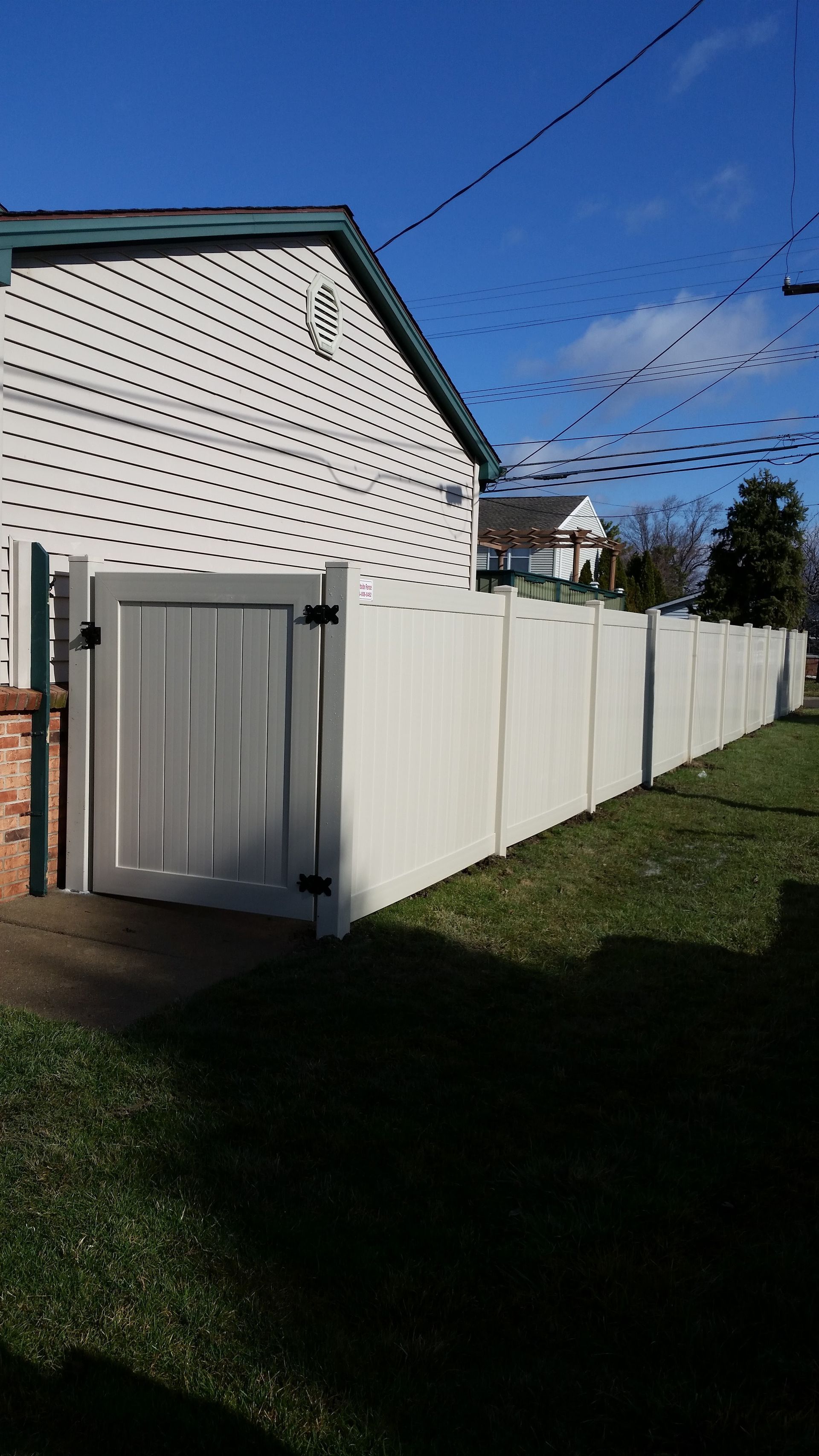 White fence and gate along a house and lawn, sunny day.