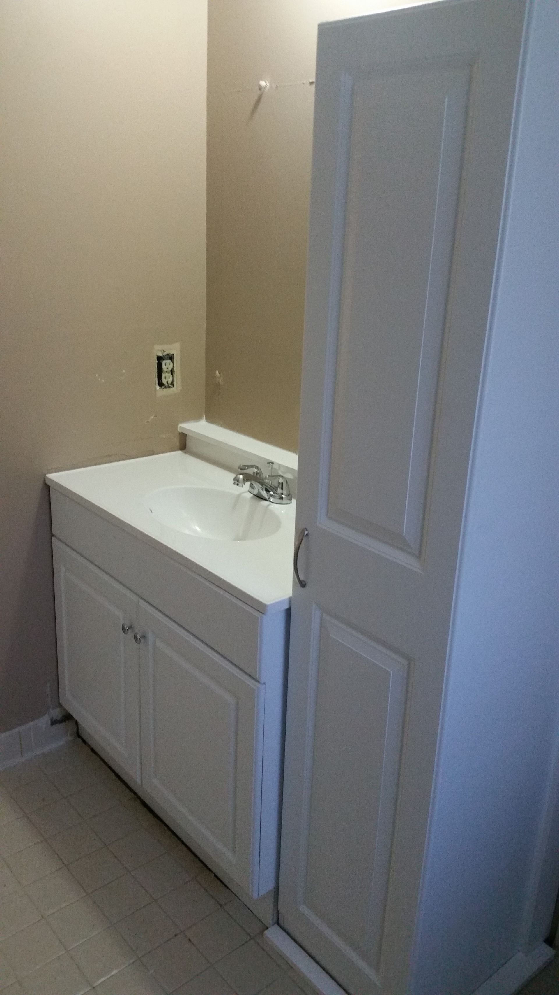 White bathroom vanity and tall cabinet in a room with tan walls and a tiled floor.