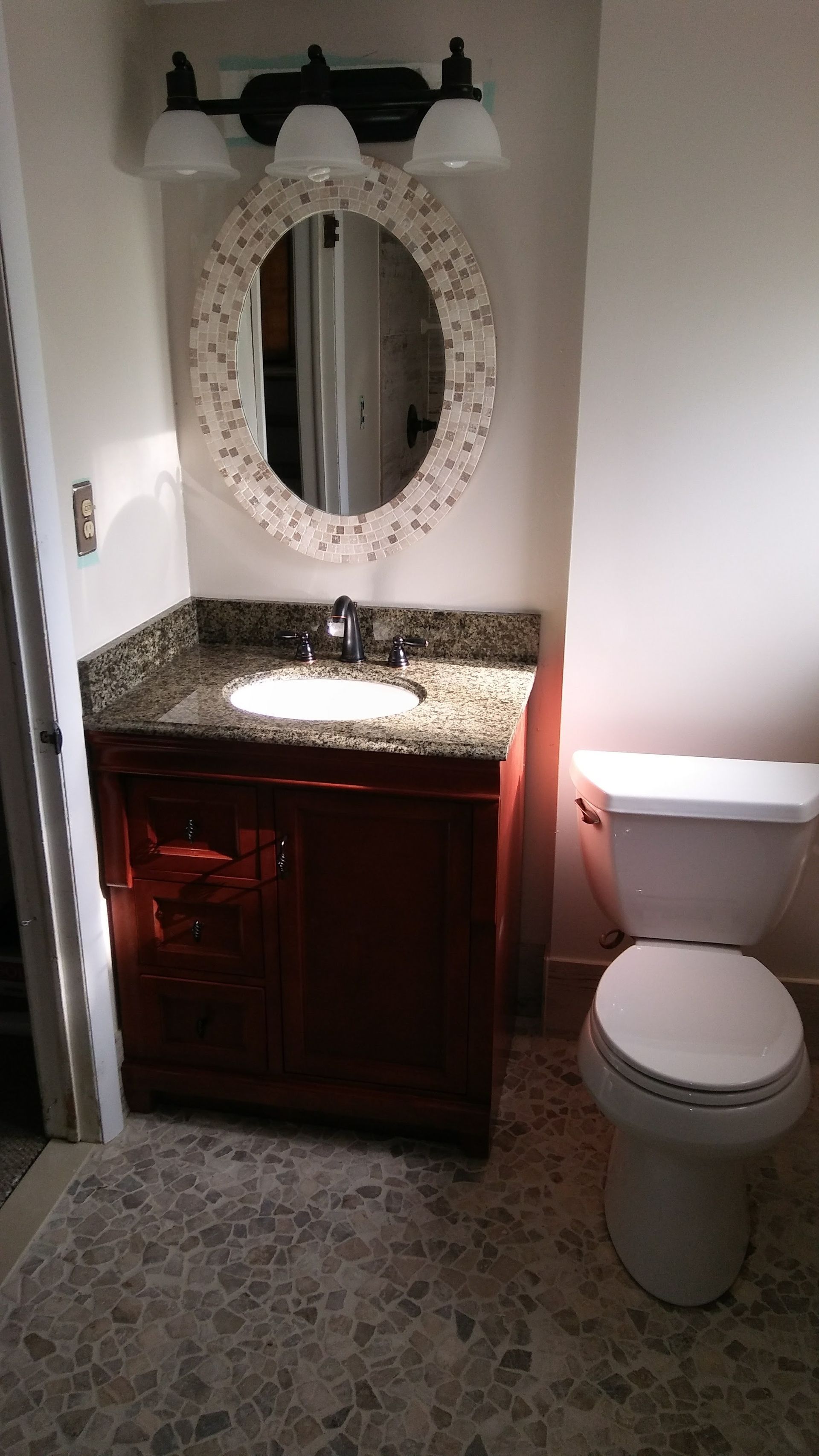 Bathroom with dark brown vanity, oval mirror, white toilet, and patterned floor.