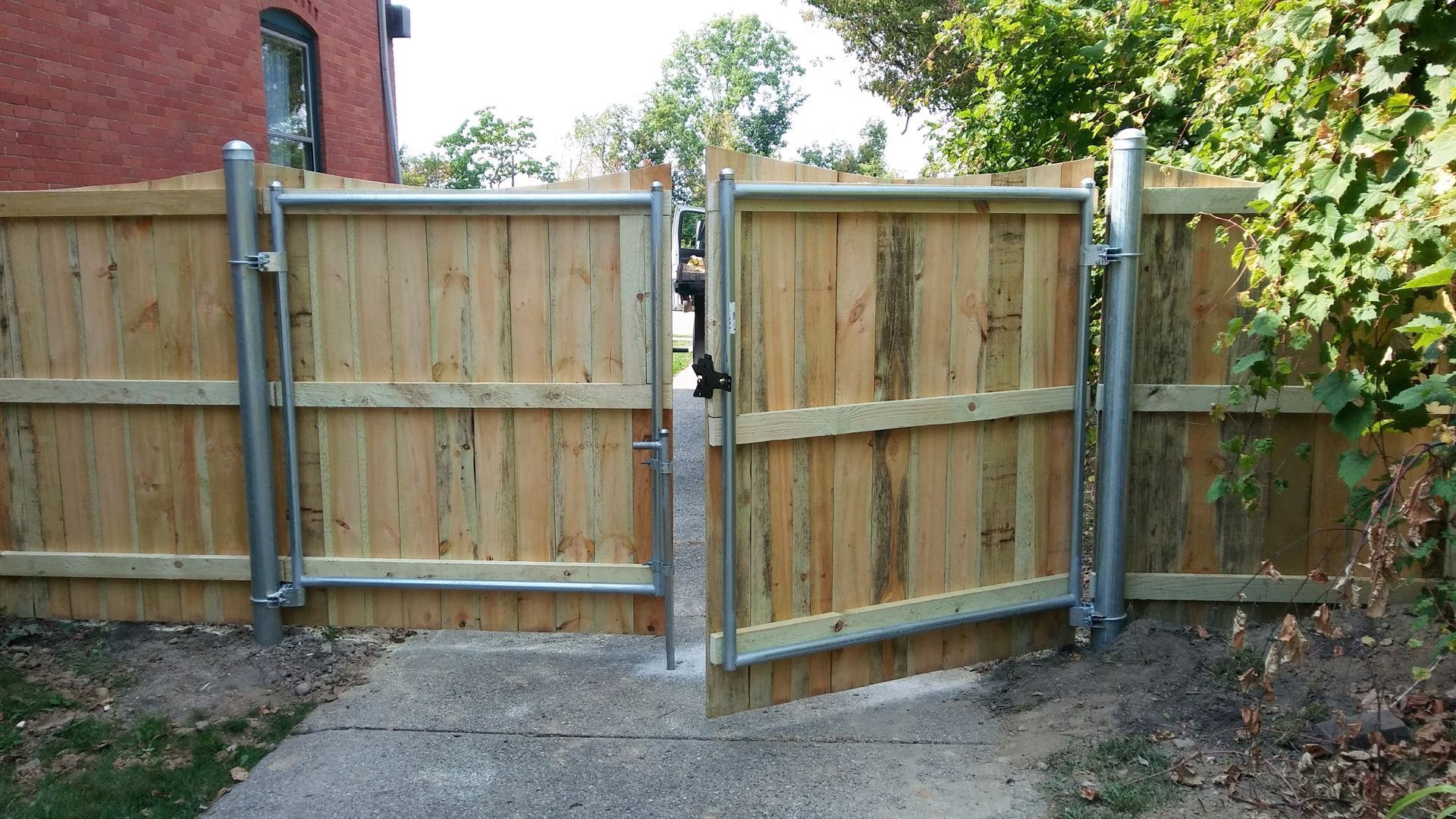 Wooden double gate in a wooden fence, partially open on a concrete path.