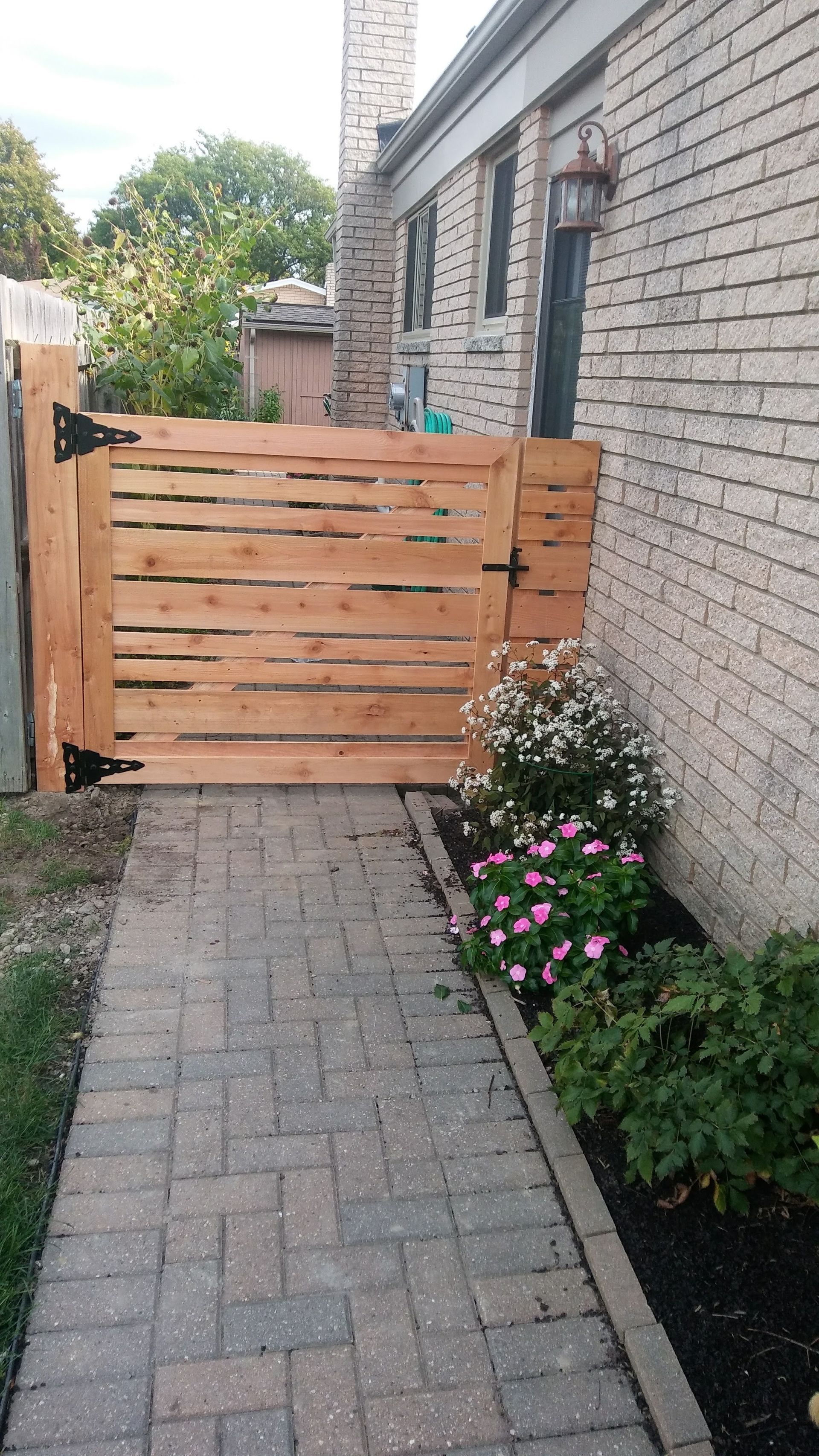 Wooden gate in a brick walkway, next to a building with pink and white flowers.