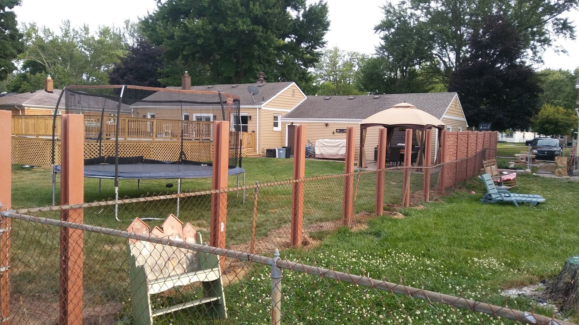 Backyard scene with fence, trampoline, gazebo, and houses in the background.