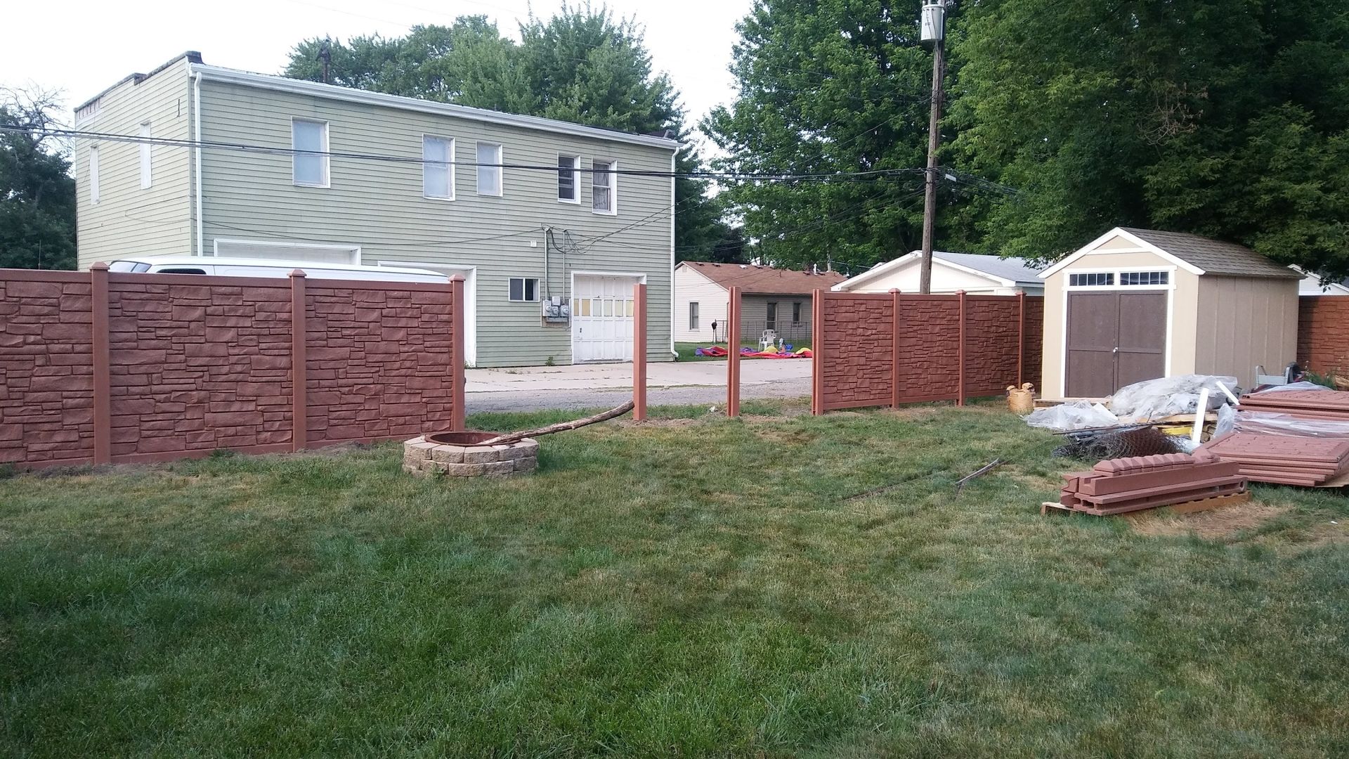 Backyard with grass, brown privacy fence, tan shed, and two-story building.