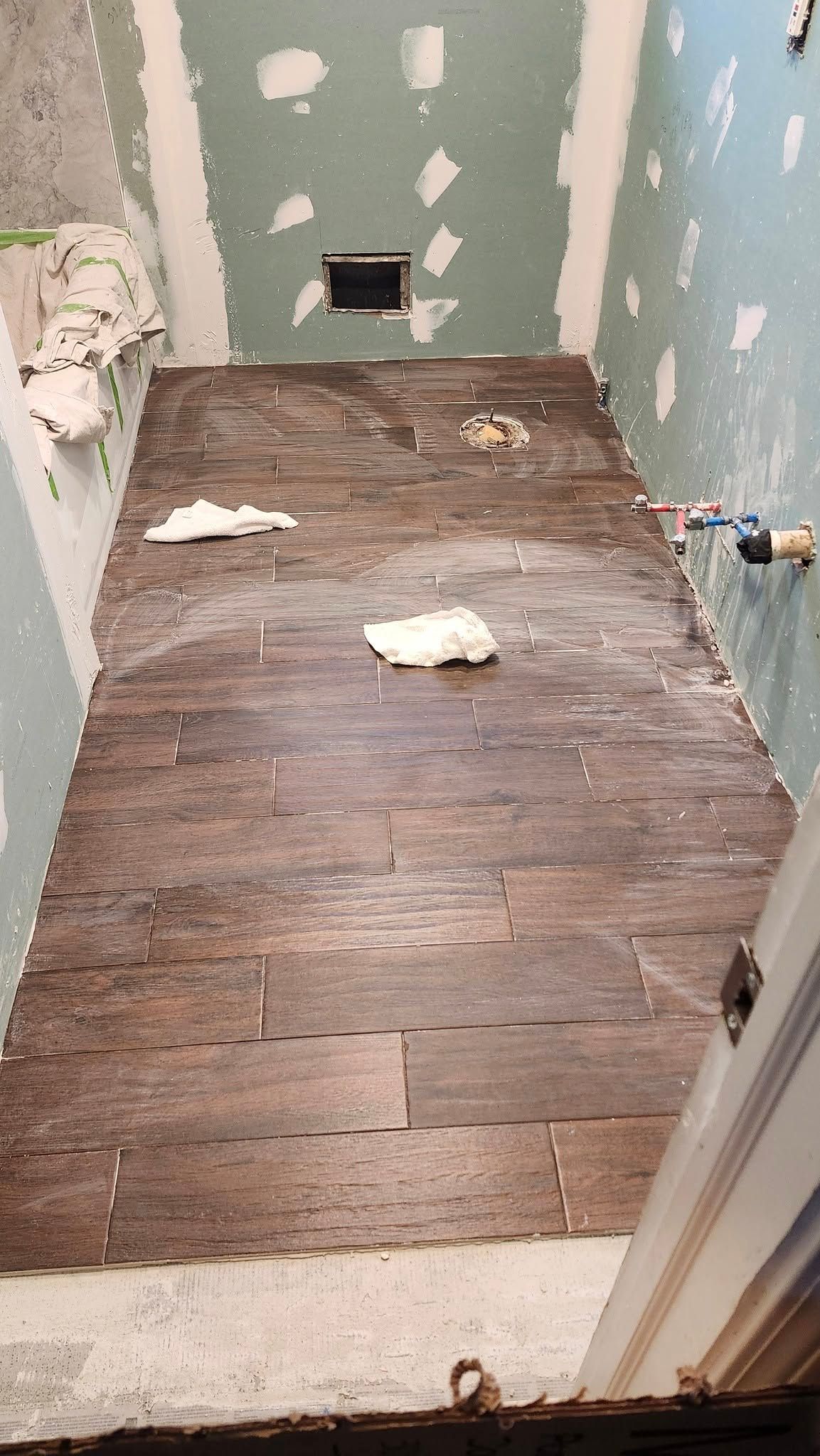 Bathroom undergoing renovation. Wood floor, exposed studs, green drywall. Door on right.