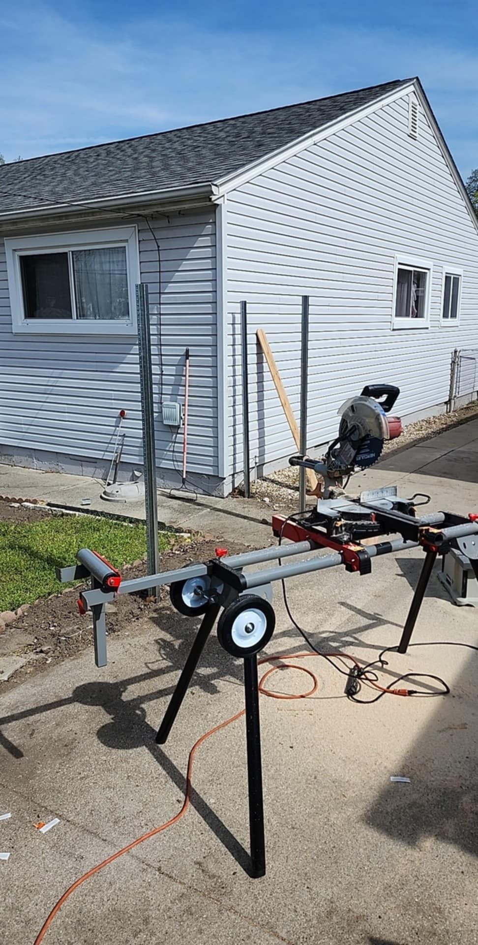 Miter saw on stand outdoors near a house with gray siding.