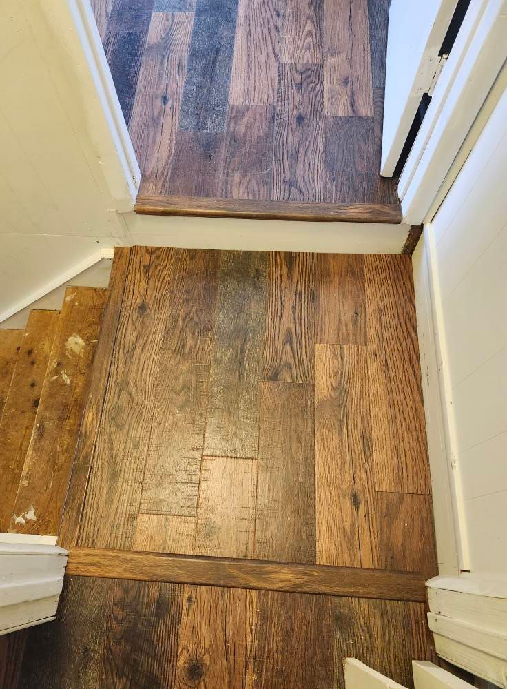 Top-down view of a landing and stairs with mismatched wood floors and brown trim.