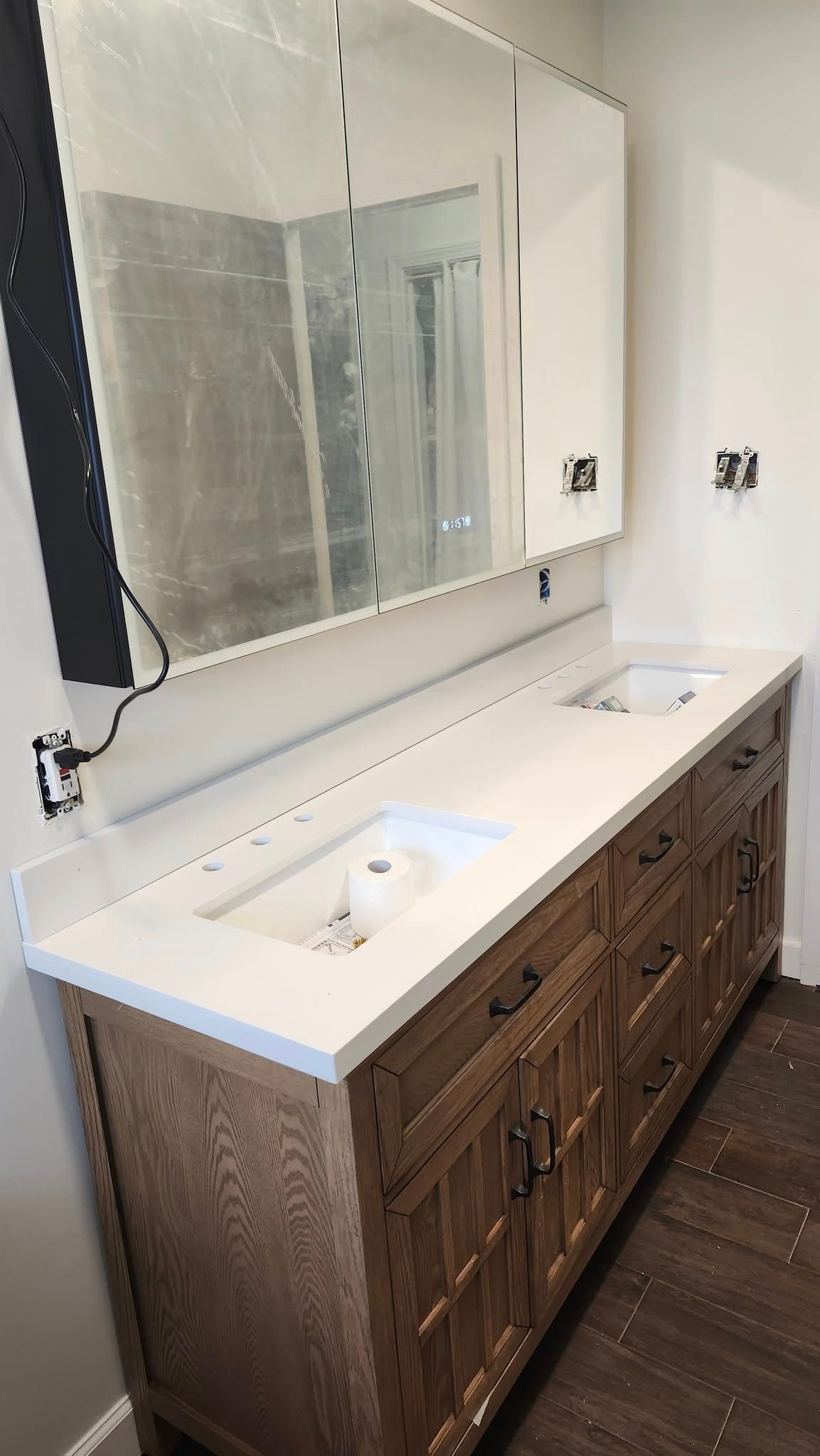 Wooden vanity with two sinks, white countertop, and large mirror in a bathroom.