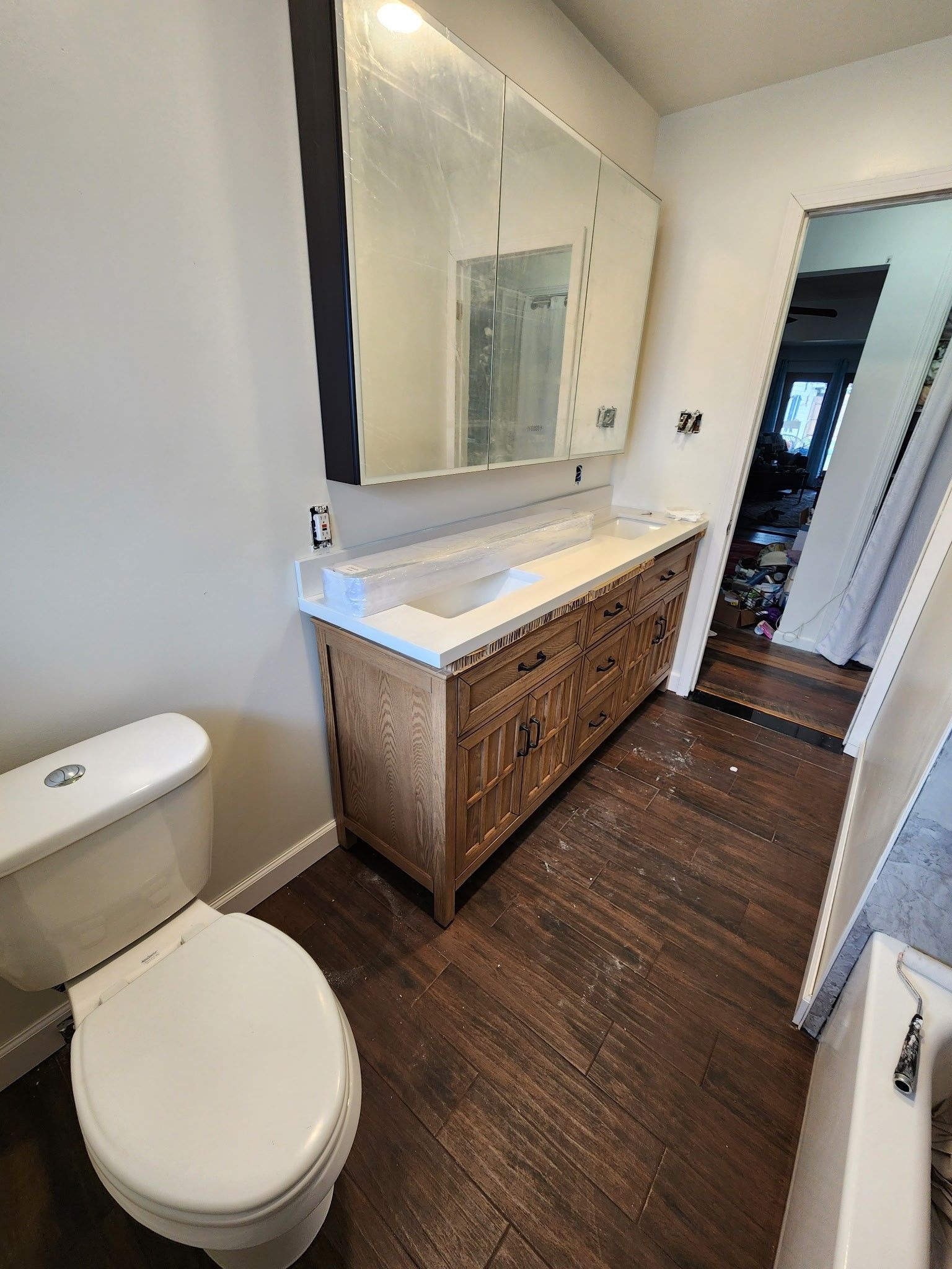 Bathroom with wooden vanity, toilet, and mirrored medicine cabinet. Dark wood flooring.