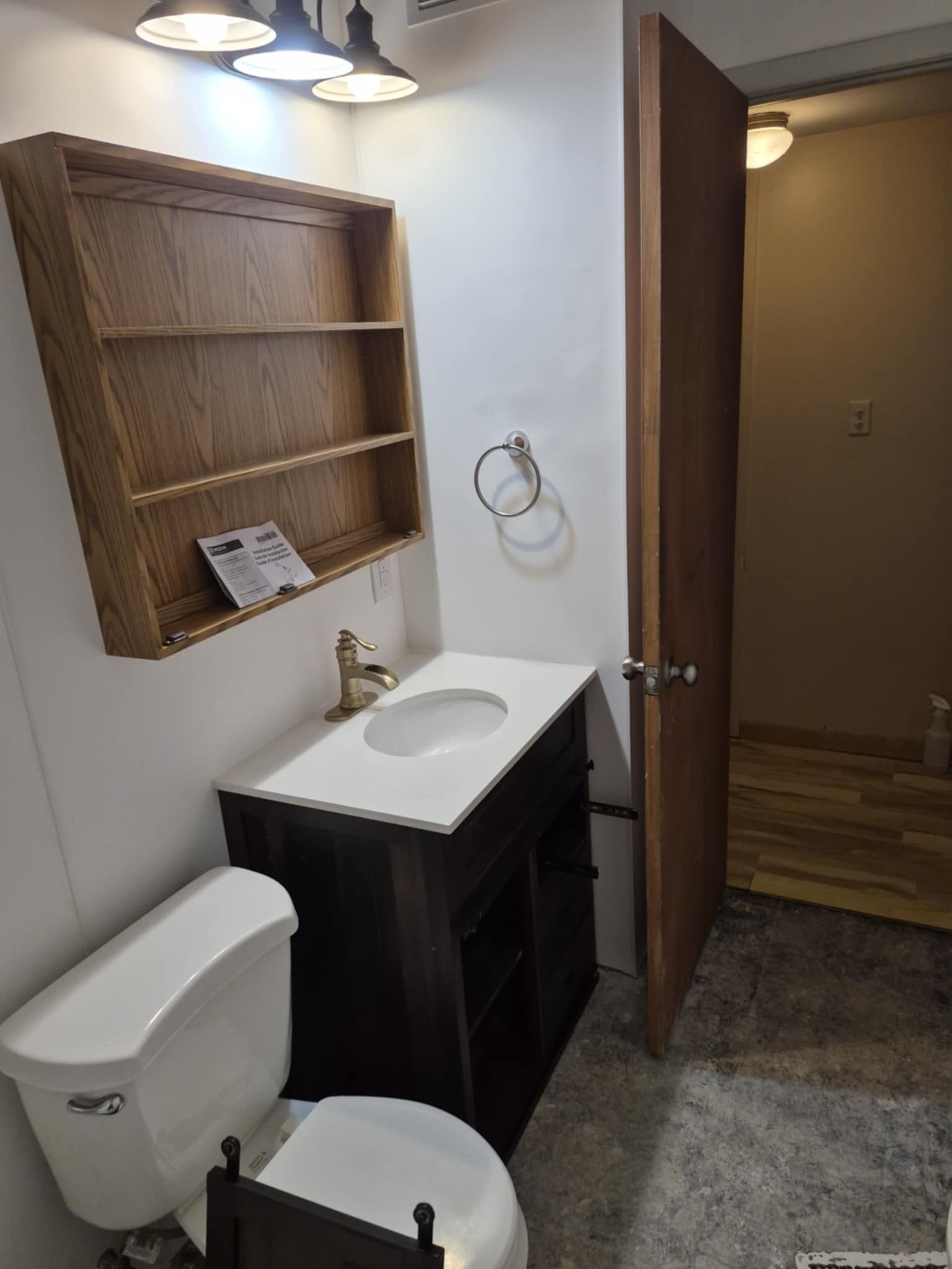Bathroom with a toilet, vanity, and open door leading to another room.