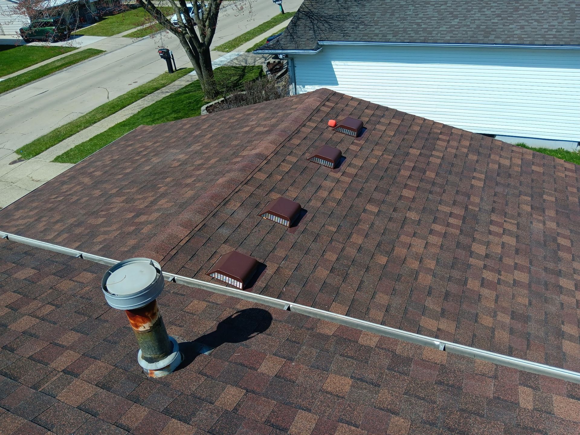 Brown shingled roof with vents and a chimney, viewed from above.