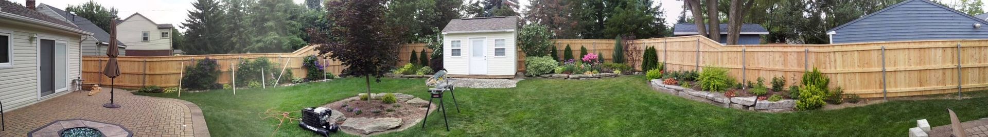 Backyard with green grass, trees, a white shed, and a brown wooden fence.