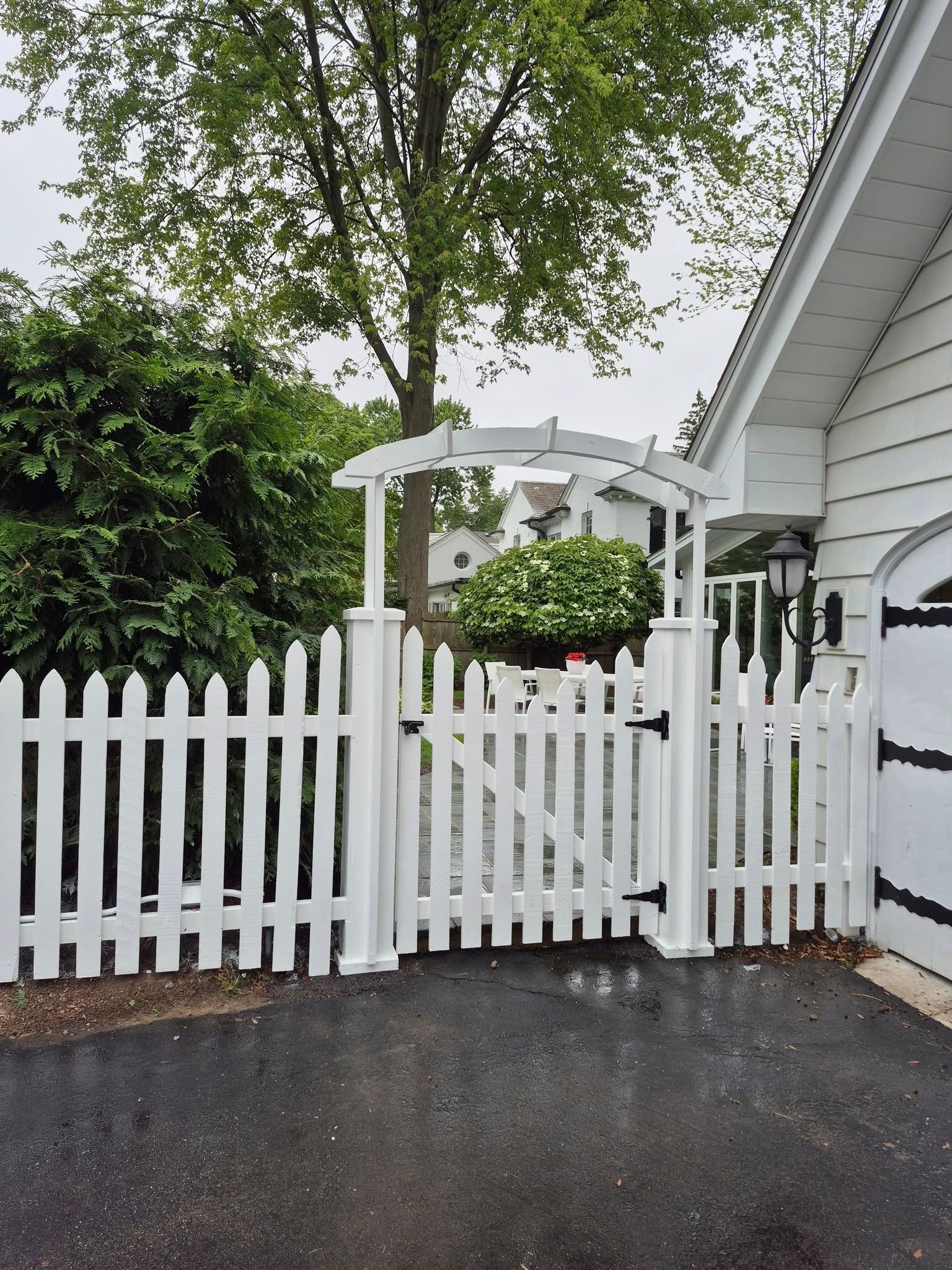 White picket fence with gate and arbor, leading to a house.