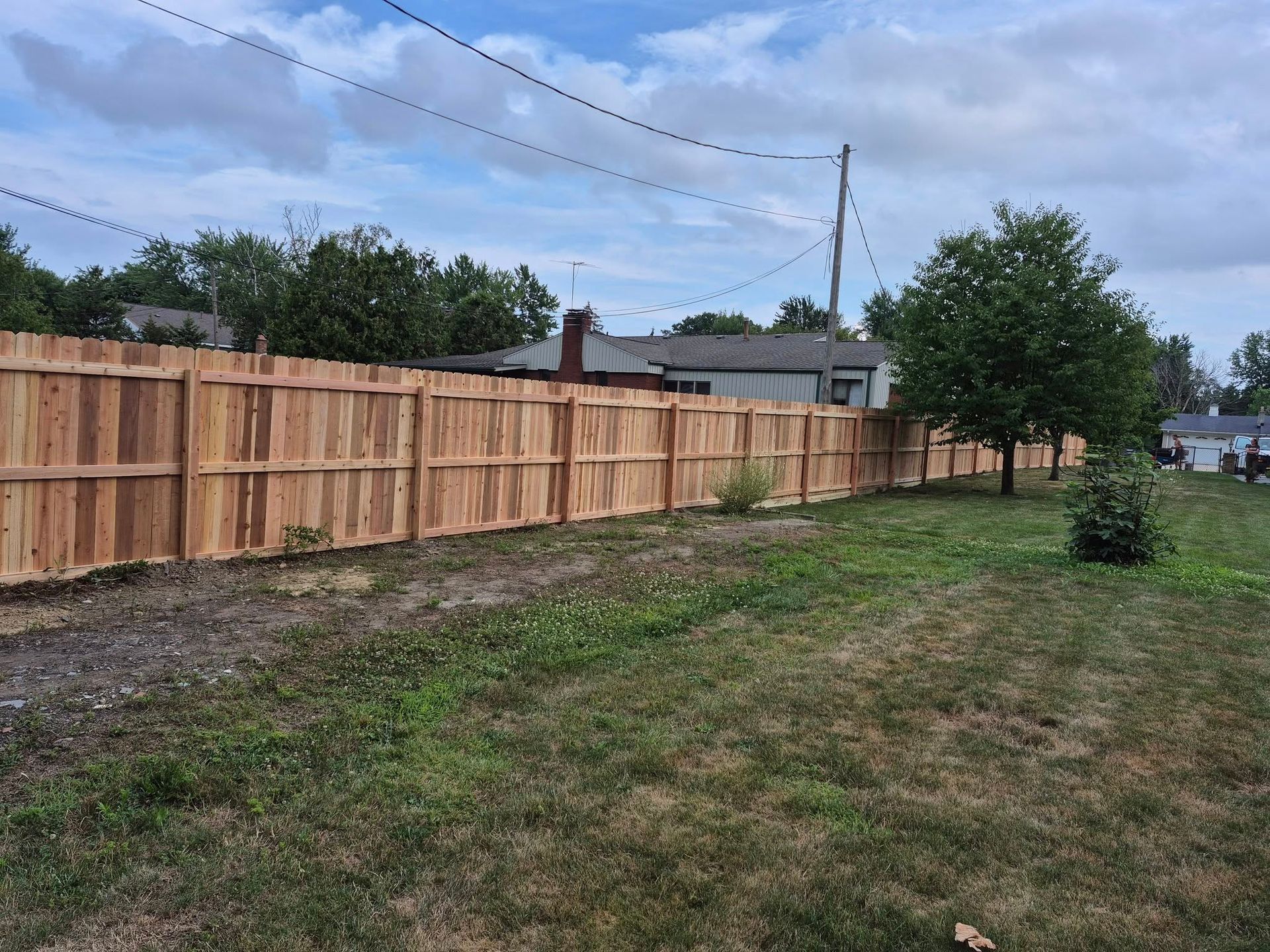 A newly built wooden fence borders a grassy yard under a cloudy sky.