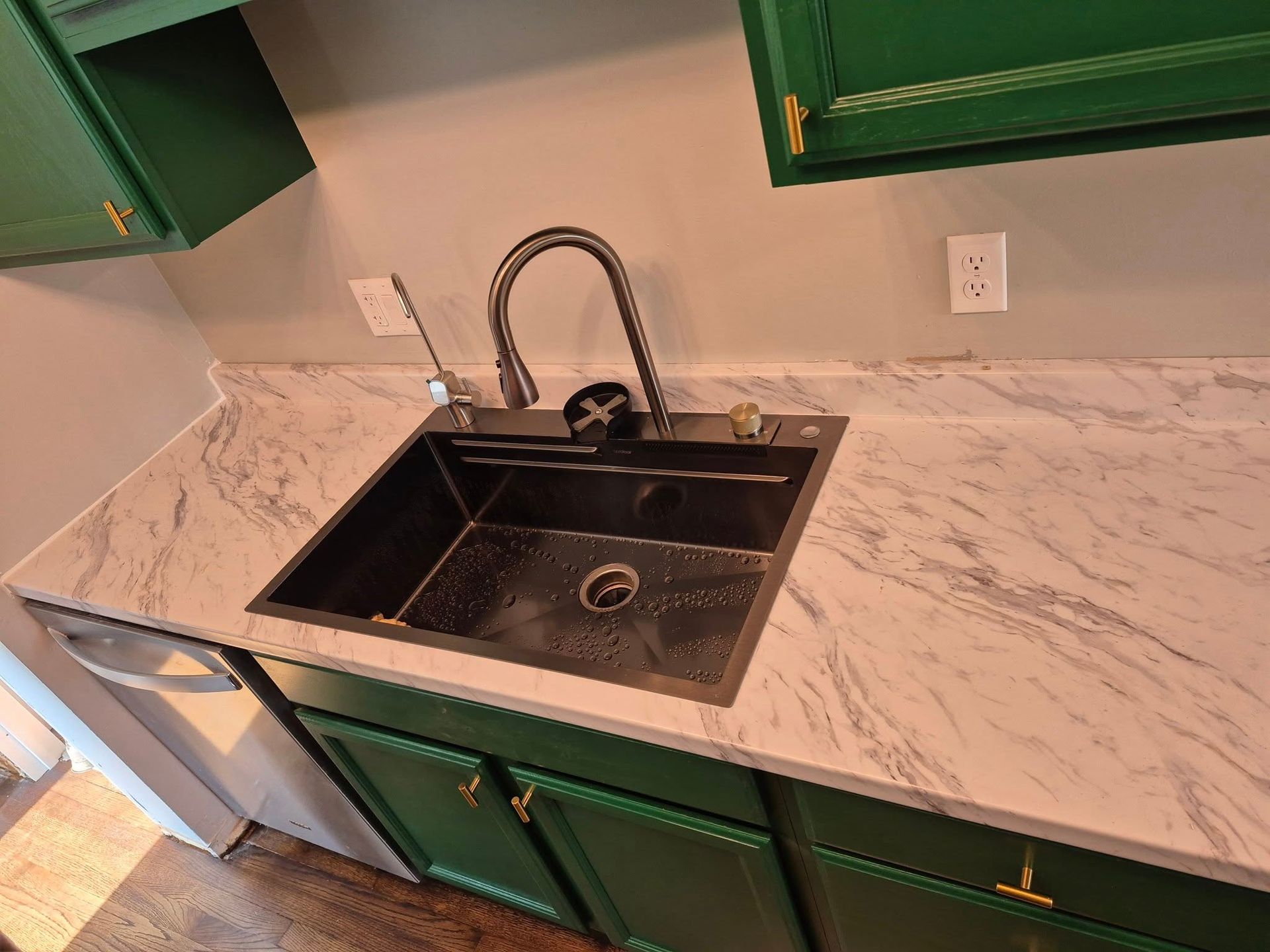 A kitchen sink with a black faucet, surrounded by white countertops and green cabinets.