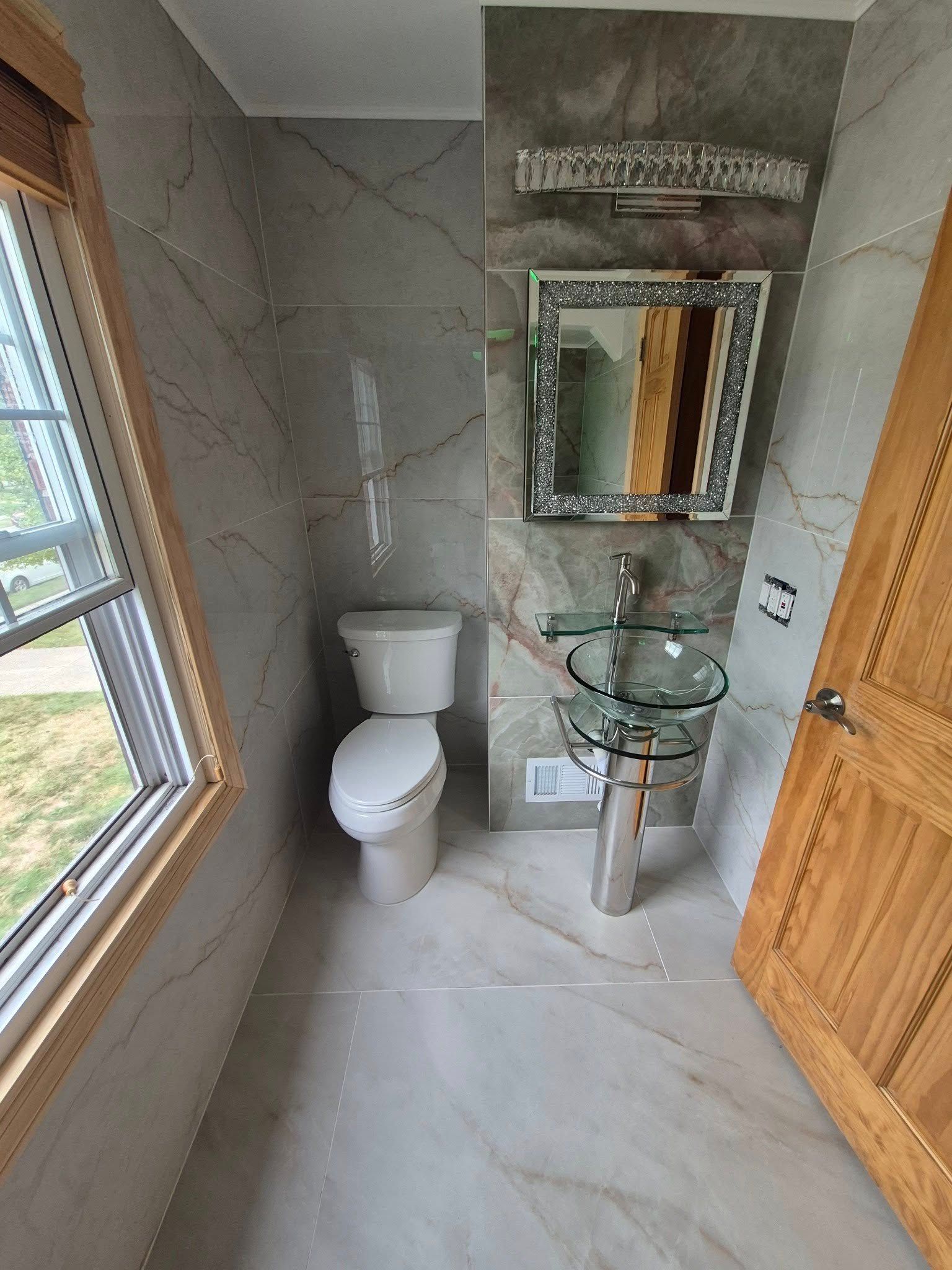 Small bathroom with grey marble tile, toilet, glass sink, and mirrored vanity.