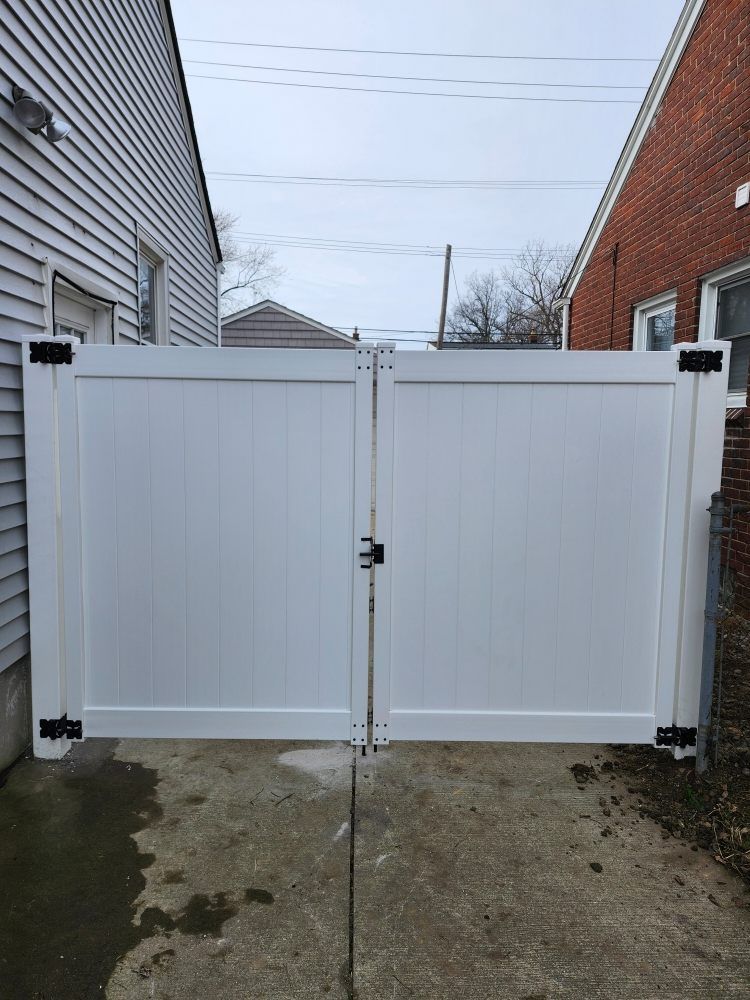 White double gate with black hinges and lock, between two buildings, concrete ground.