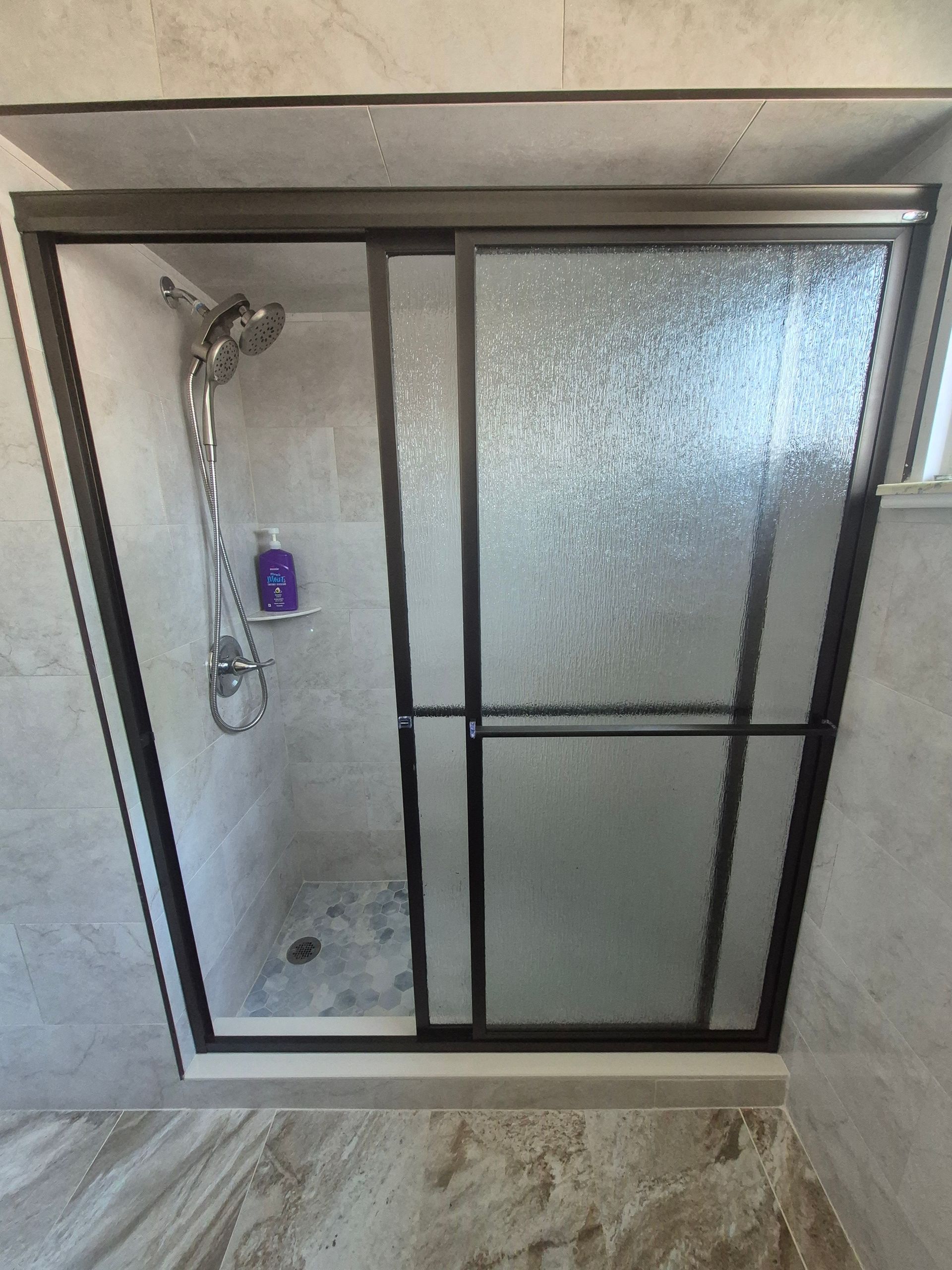 Shower with frosted glass sliding doors, gray frame, chrome showerhead, and shampoo bottle.