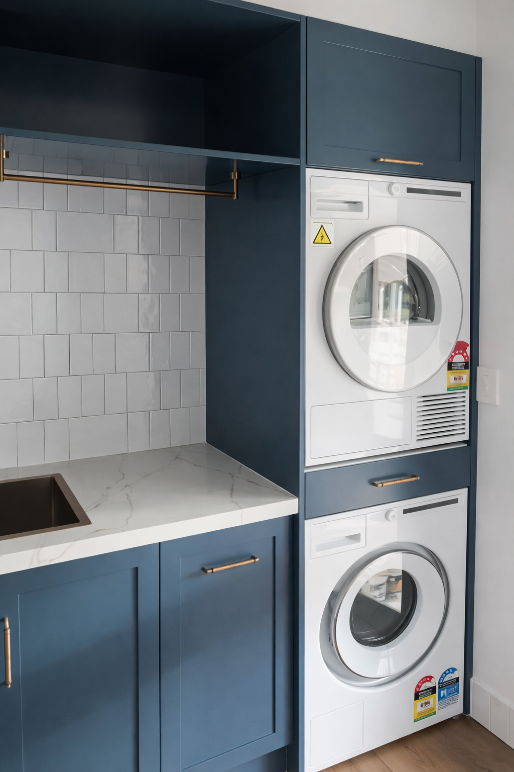 Blue laundry room with stacked washer/dryer, sink, and tiled backsplash — Paul Tagget Kitchens In Goonellabah, NSW