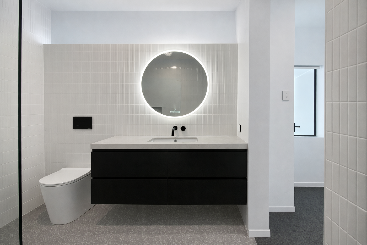 Modern bathroom with black vanity, round mirror, and white tiled walls — Paul Tagget Kitchens In Goonellabah, NSW