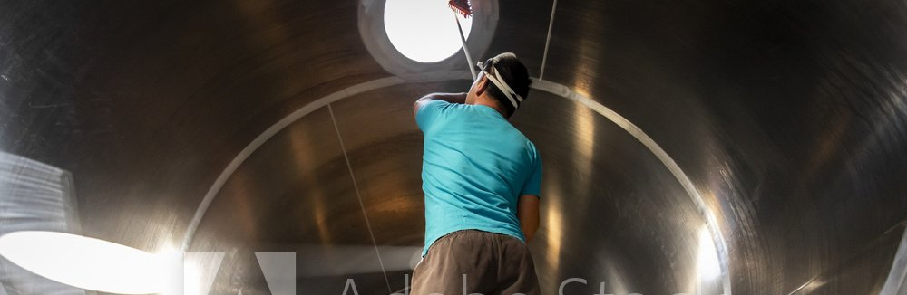 Person in a blue shirt reaching up inside a large metal tunnel or pipe.