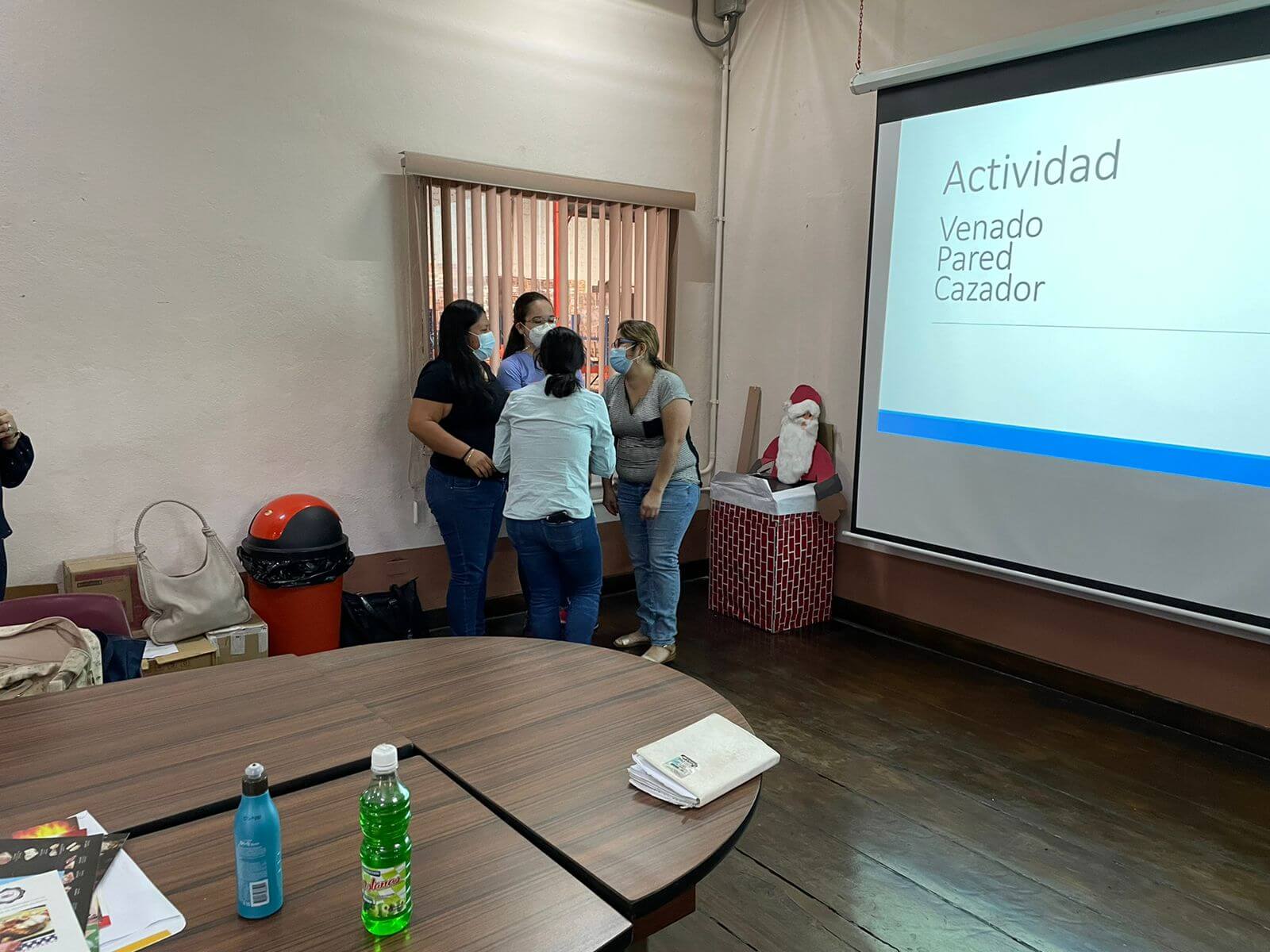 Grupo de personas reunidas, interactuando cerca de una ventana y una pantalla proyectada que mostraba palabras en español.