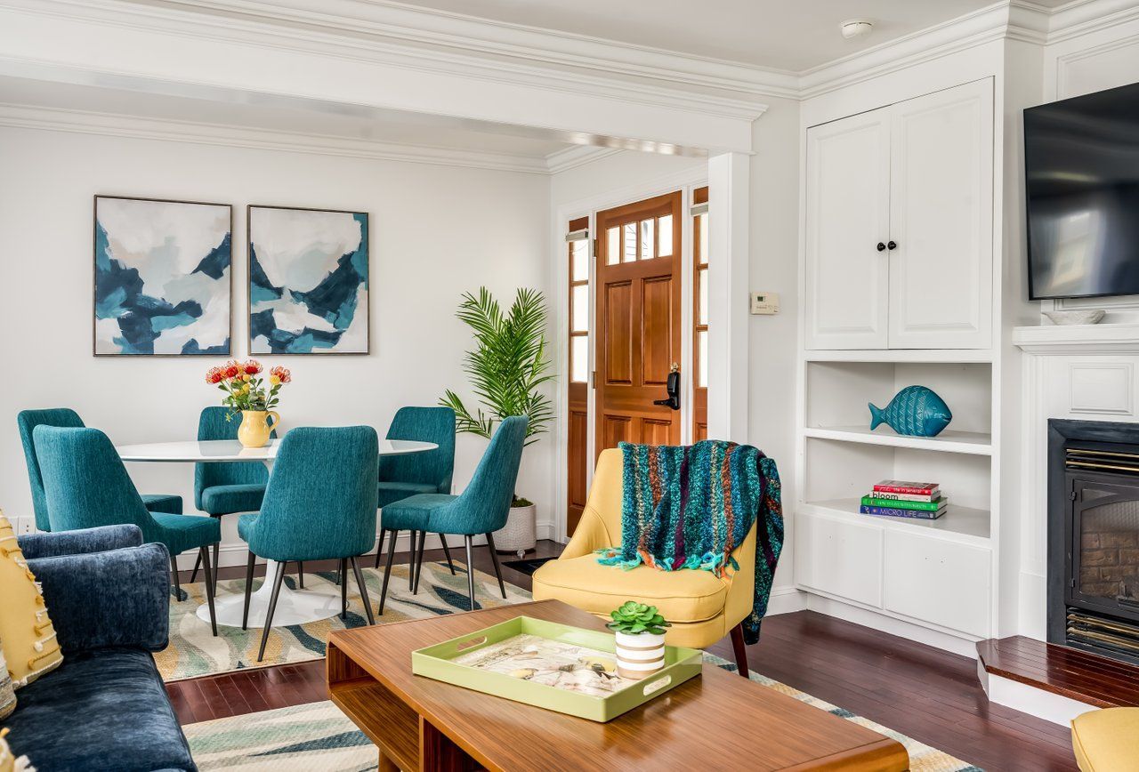 Bright living room with a yellow armchair, teal dining chairs, wood coffee table, and white built-in shelves near a door.