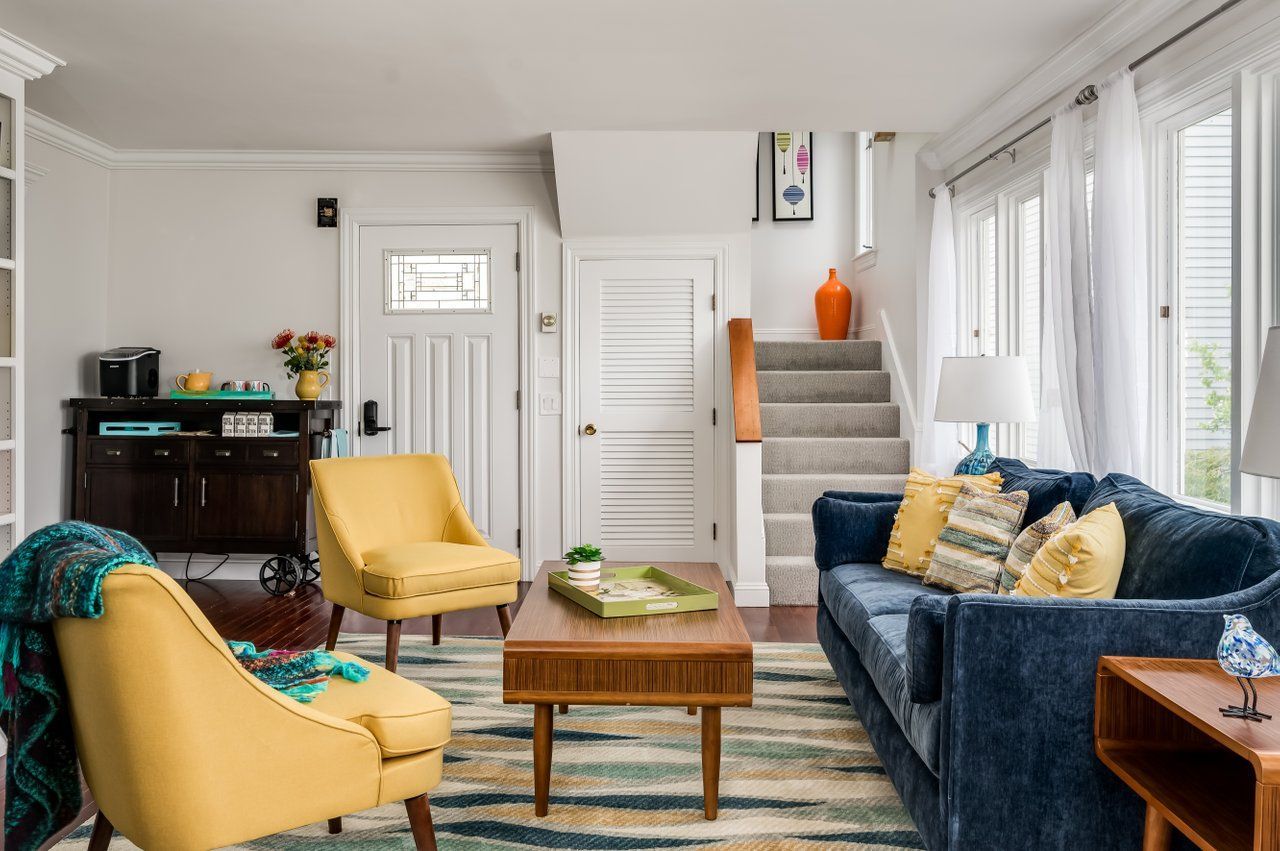 A living room featuring two yellow chairs, a blue couch, a wooden coffee table, and a staircase leading to an upper floor.