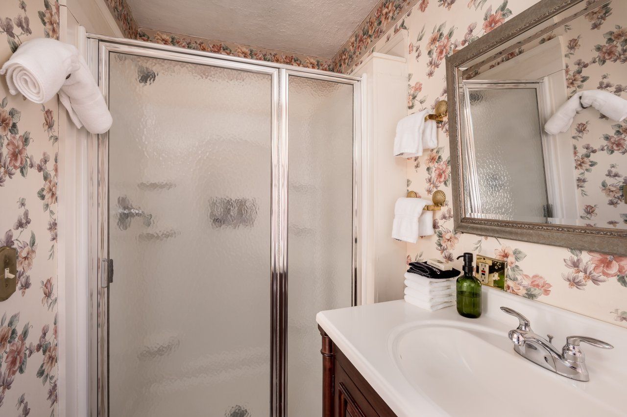 A bathroom featuring a shower stall with glass doors, a vanity sink, and walls covered in floral wallpaper.