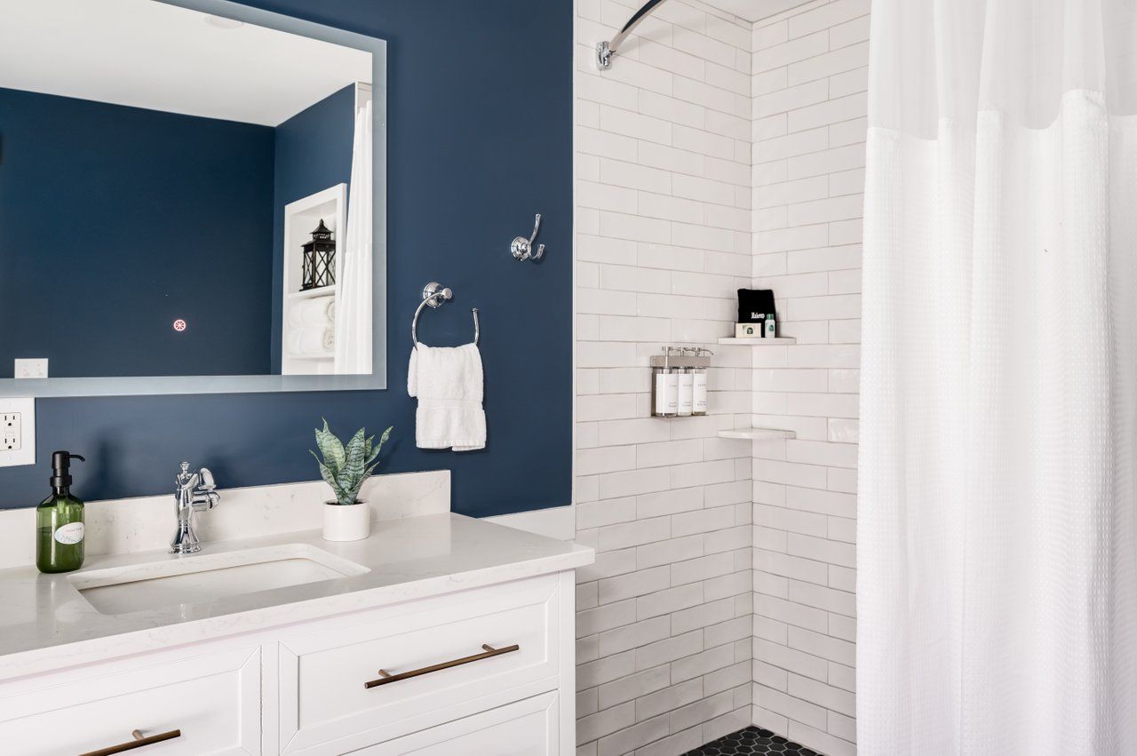 A modern bathroom featuring a white vanity with a blue wall, a mirror, and a tiled shower with a white curtain.