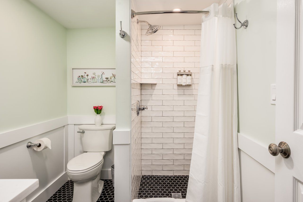 A bathroom featuring a toilet, a walk-in shower with white subway tiles, and a white vanity against light green walls.