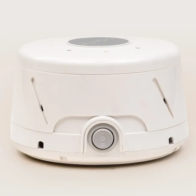 A white Yogasleep Dohm classic sound machine with a center power switch and side slots for adjustable white noise.
