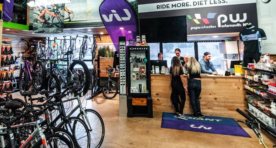 Bicycle shop interior with staff assisting customers at a wooden counter, surrounded by bikes for sale.
