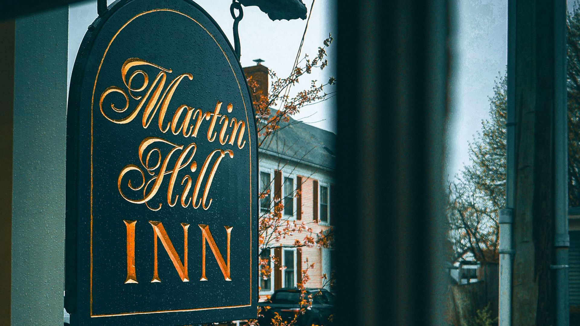 Martin Hill Inn sign on a post, dark green with gold lettering, beside a street in winter.