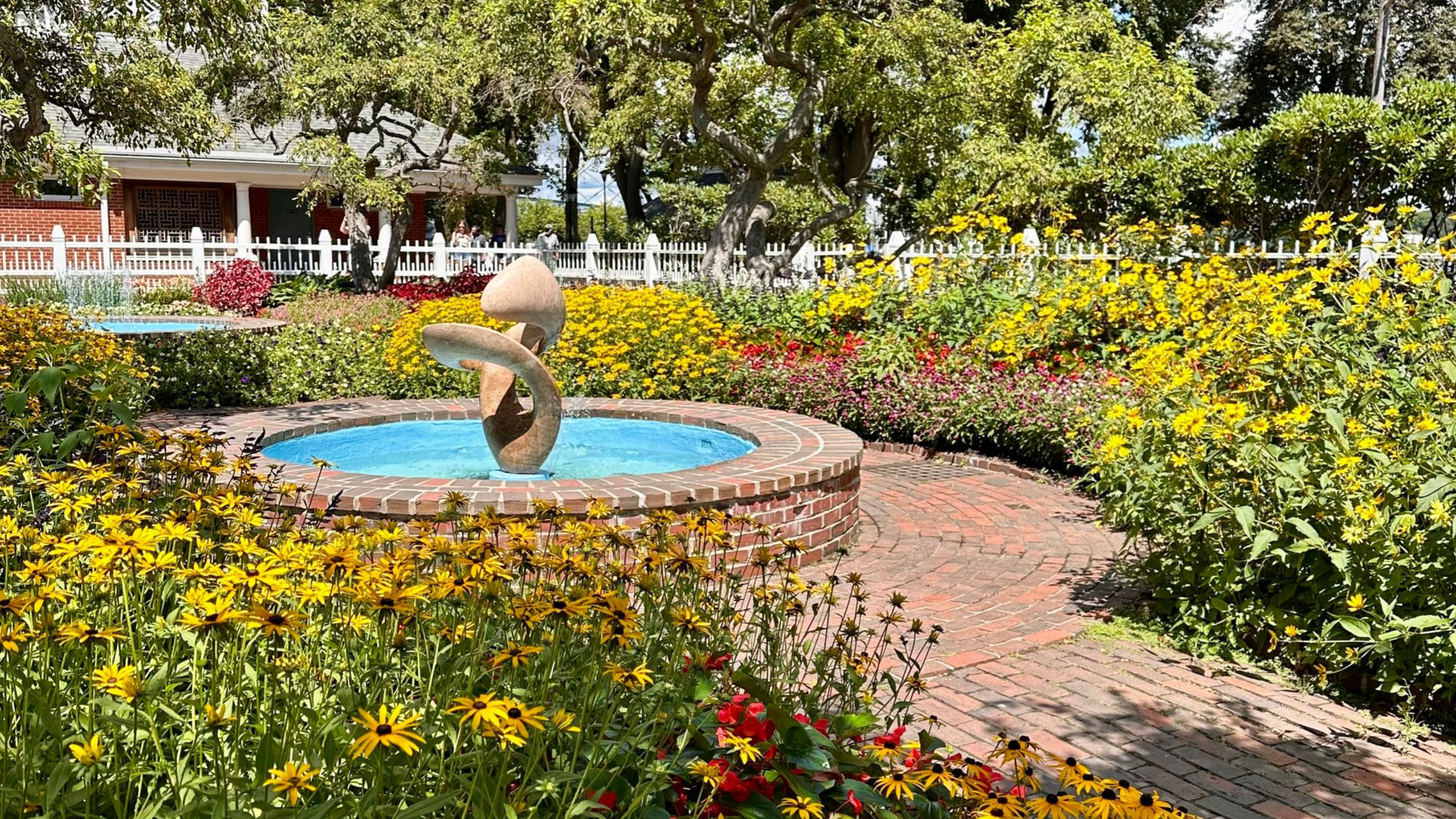 Garden fountain with blue water, brick path, and colorful yellow and red flowers in bloom
