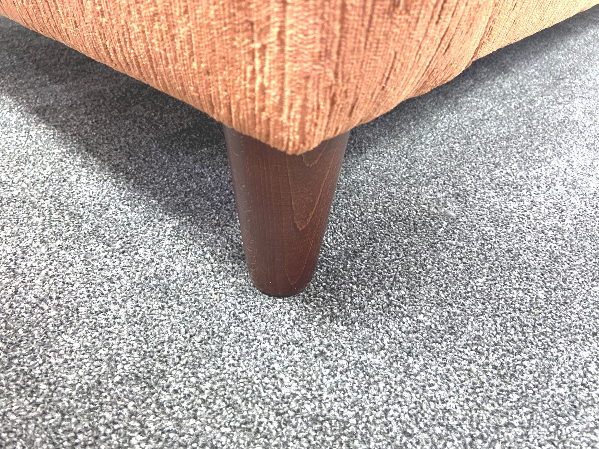 A brown couch with wooden legs is sitting on a gray carpet.