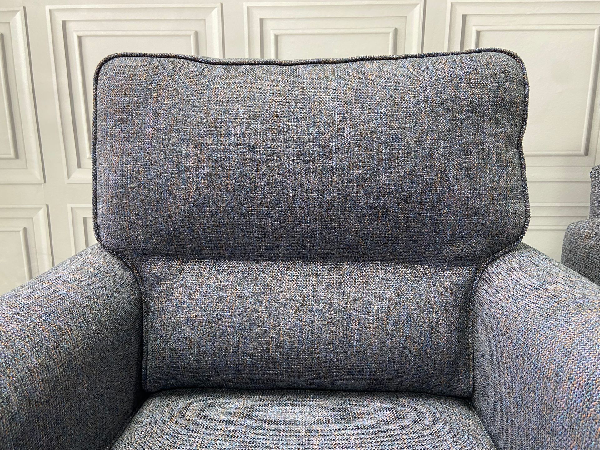 A close up of a gray chair with a white wall in the background.