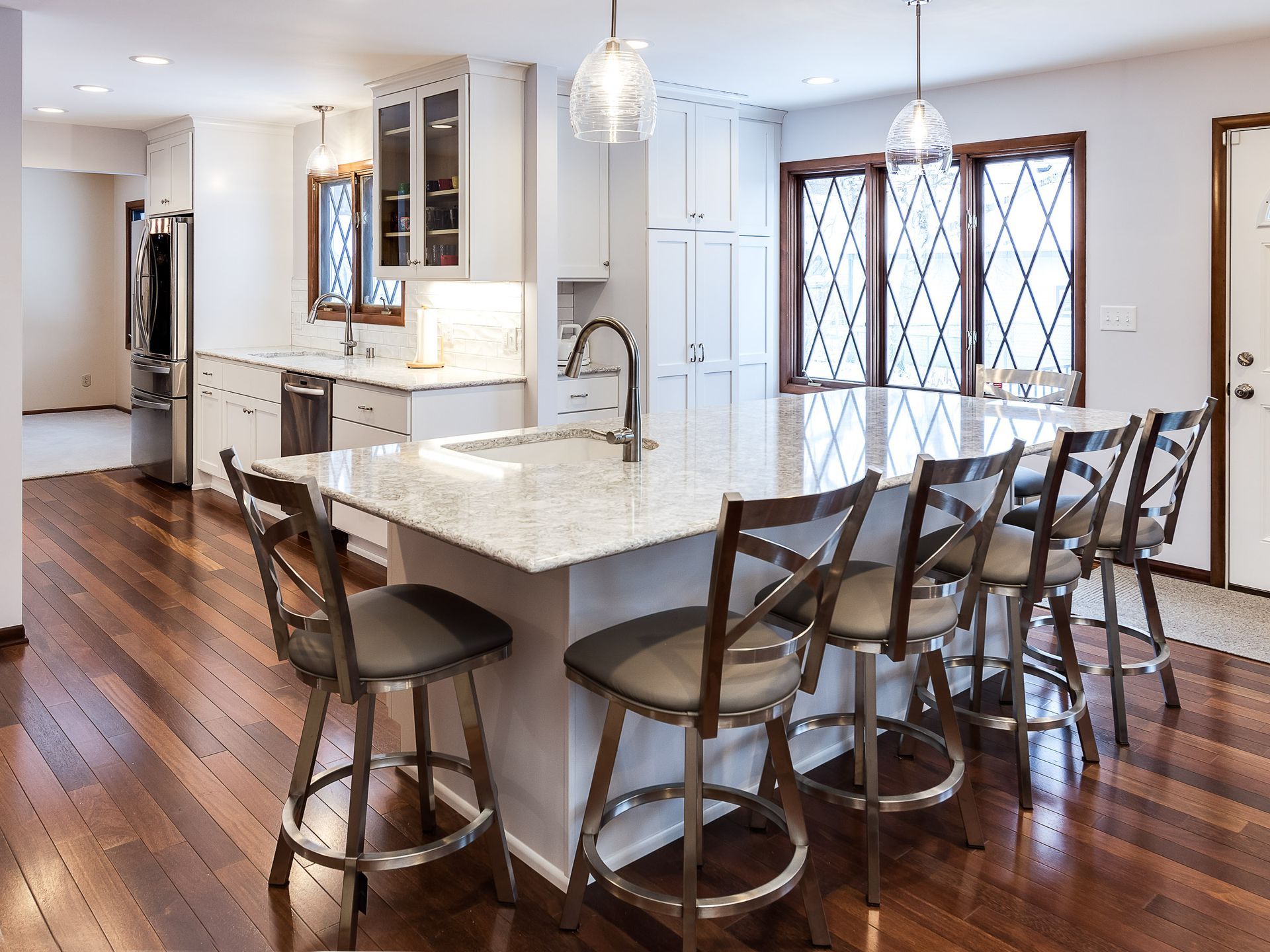 Modern kitchen with white cabinets, island with stools, and dark wood floors.
