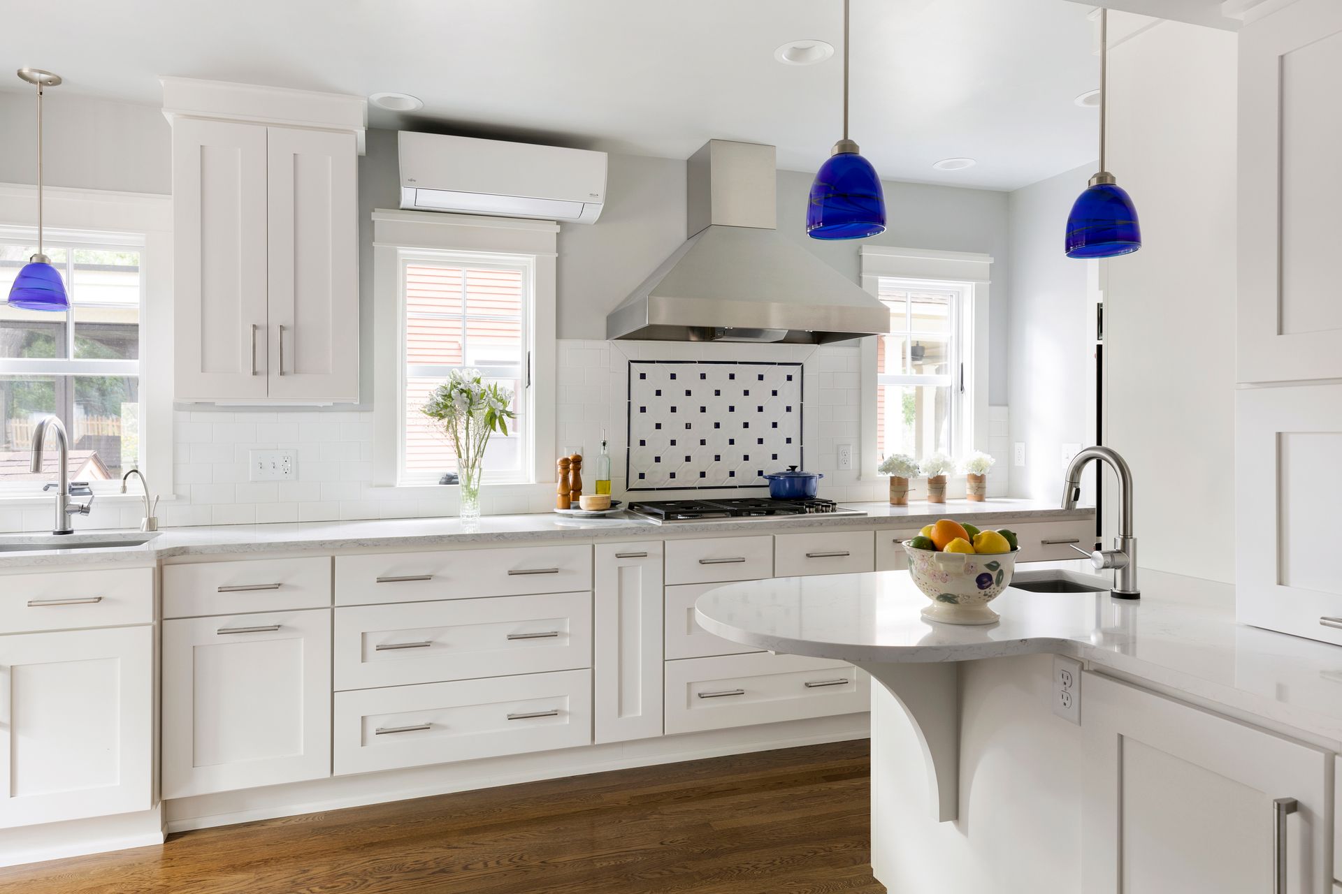 White kitchen with wooden floor, white cabinets, island, blue pendant lights.